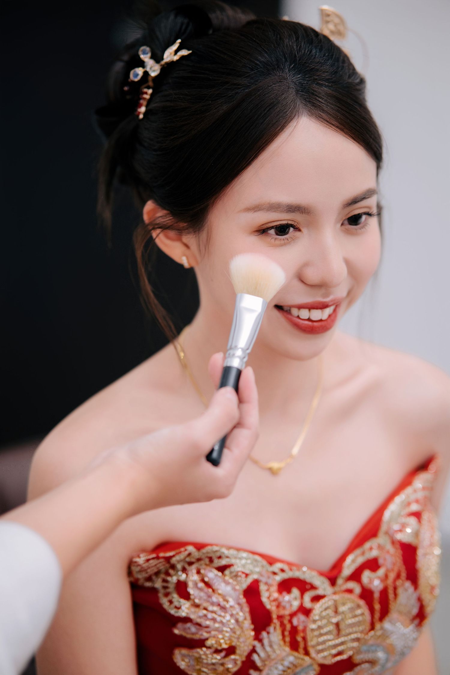 A person in a red traditional dress applies makeup with a brush in a series of close-up shots.