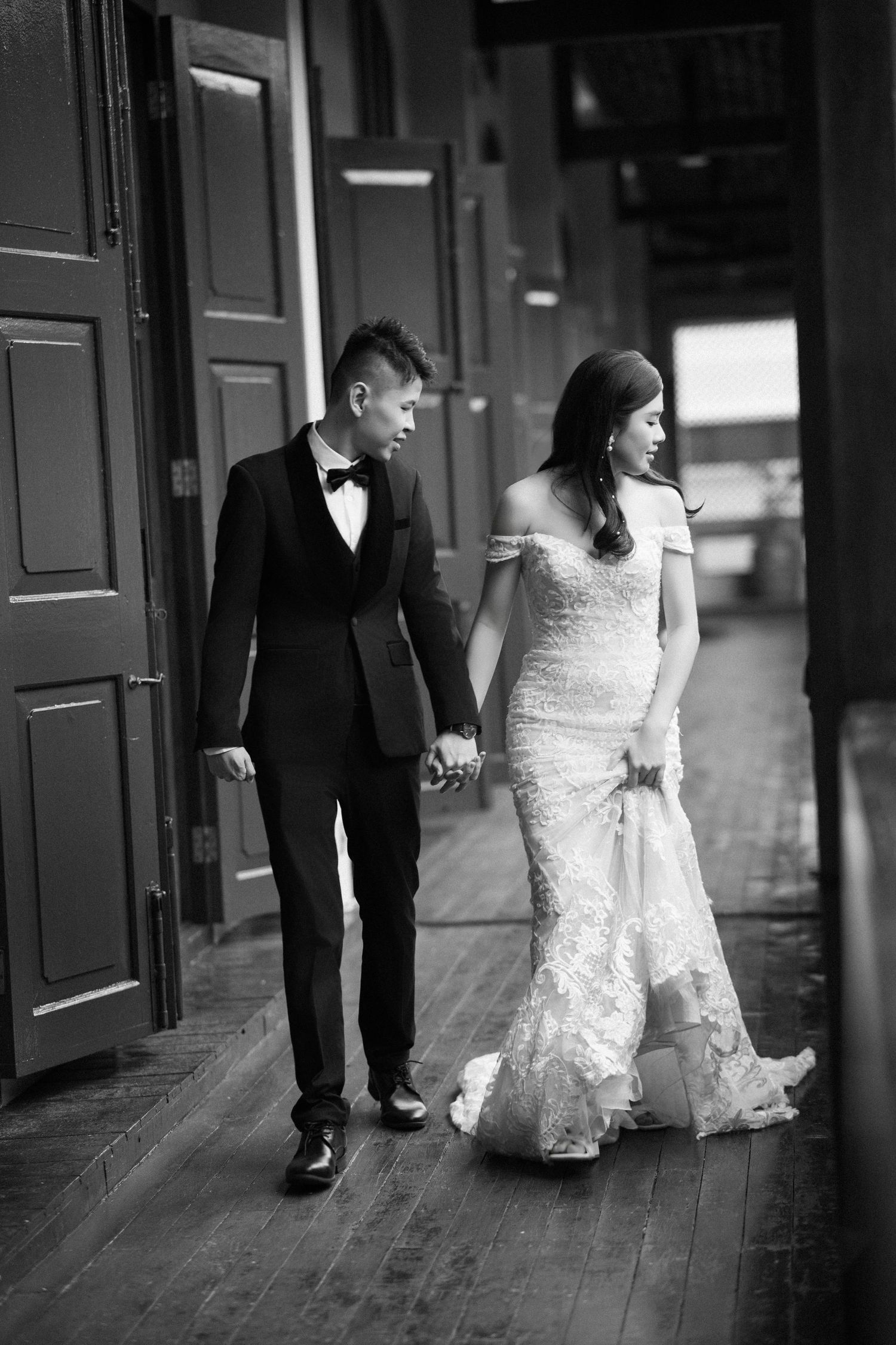 Candid black and white wedding portrait of a groom leading his bride along the Seven Terraces heritage balcony