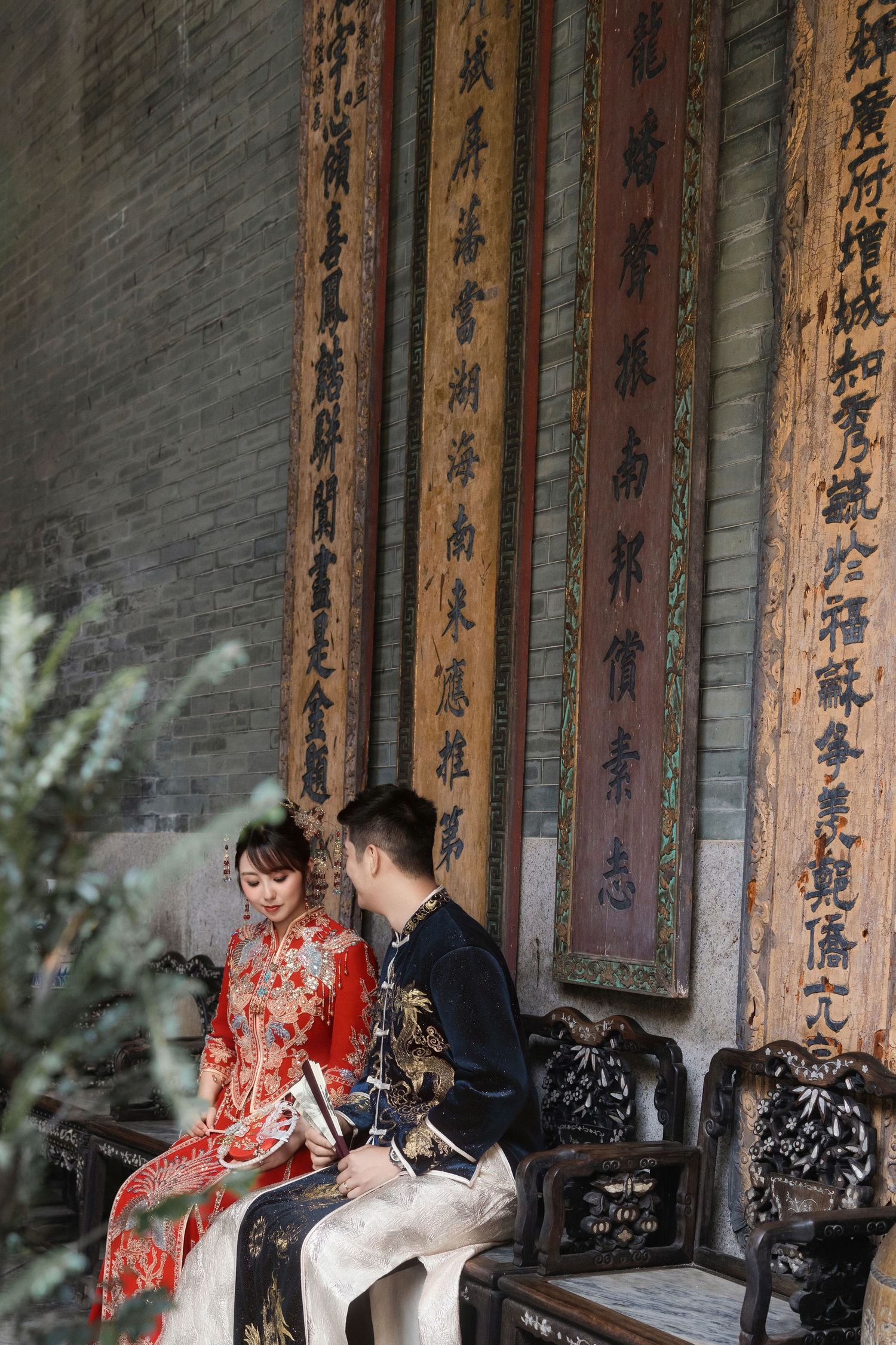 Side profile of a bride in a red Xiu He Fu sitting next to a groom in a navy dragon robe