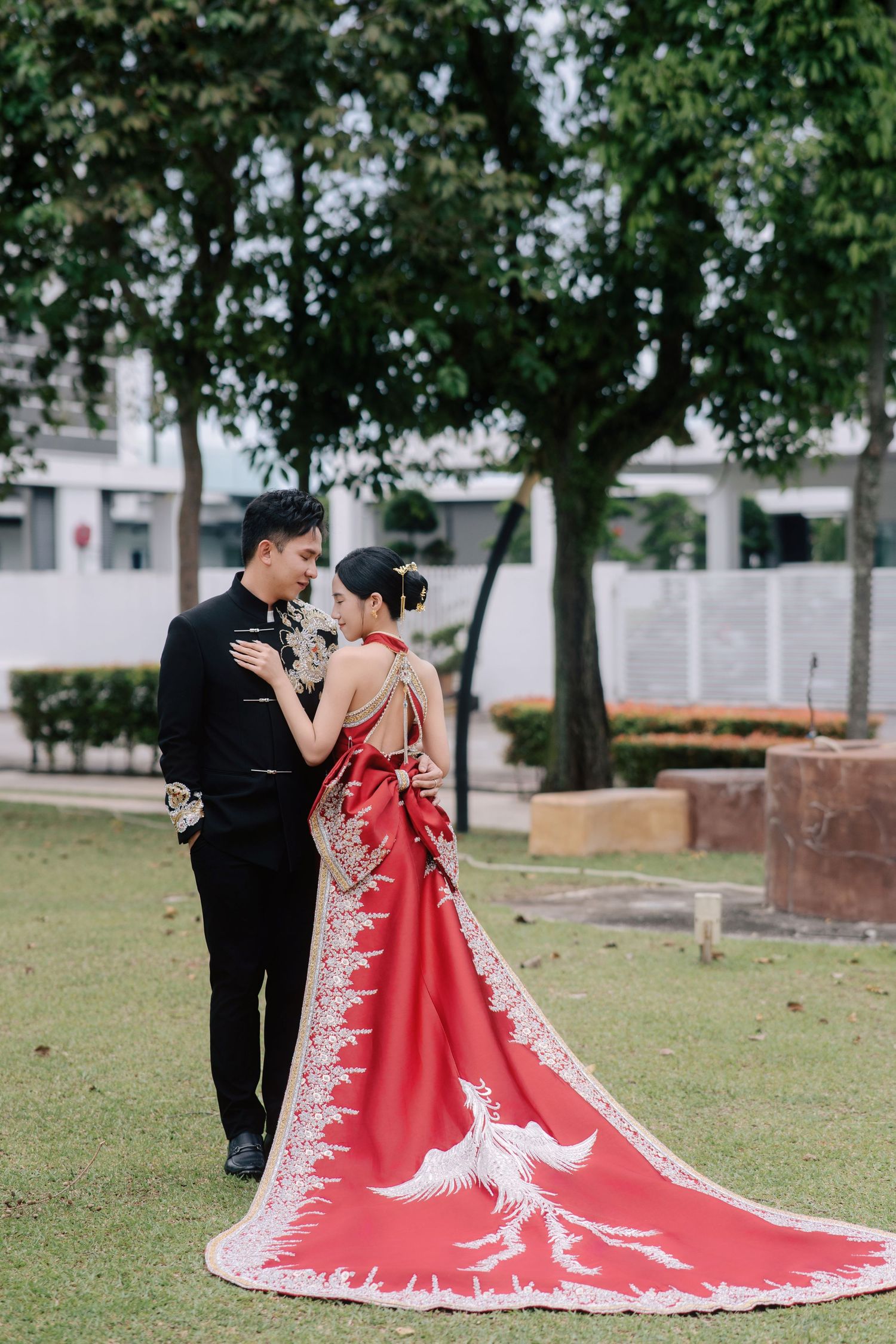 Groom embracing the bride from behind, showcasing her red qipao's open back and long phoenix-tail train
