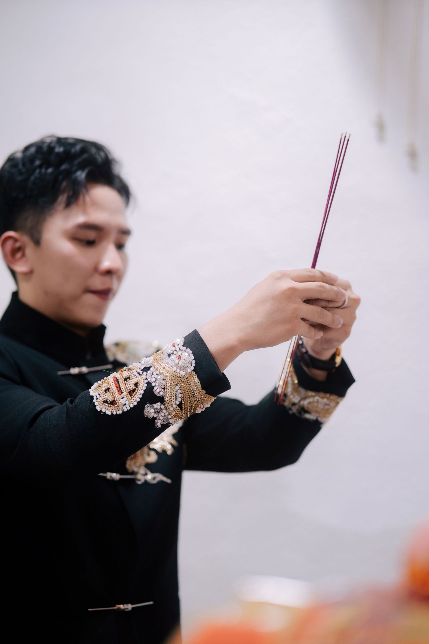 Groom holding incense sticks while wearing a black and gold robe for a traditional Chinese wedding prayer