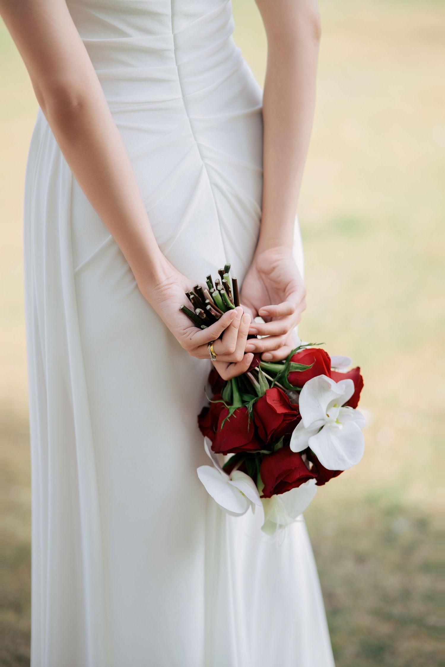 Close-up of hands holding a red and white bridal bouquet against a white wedding dress.