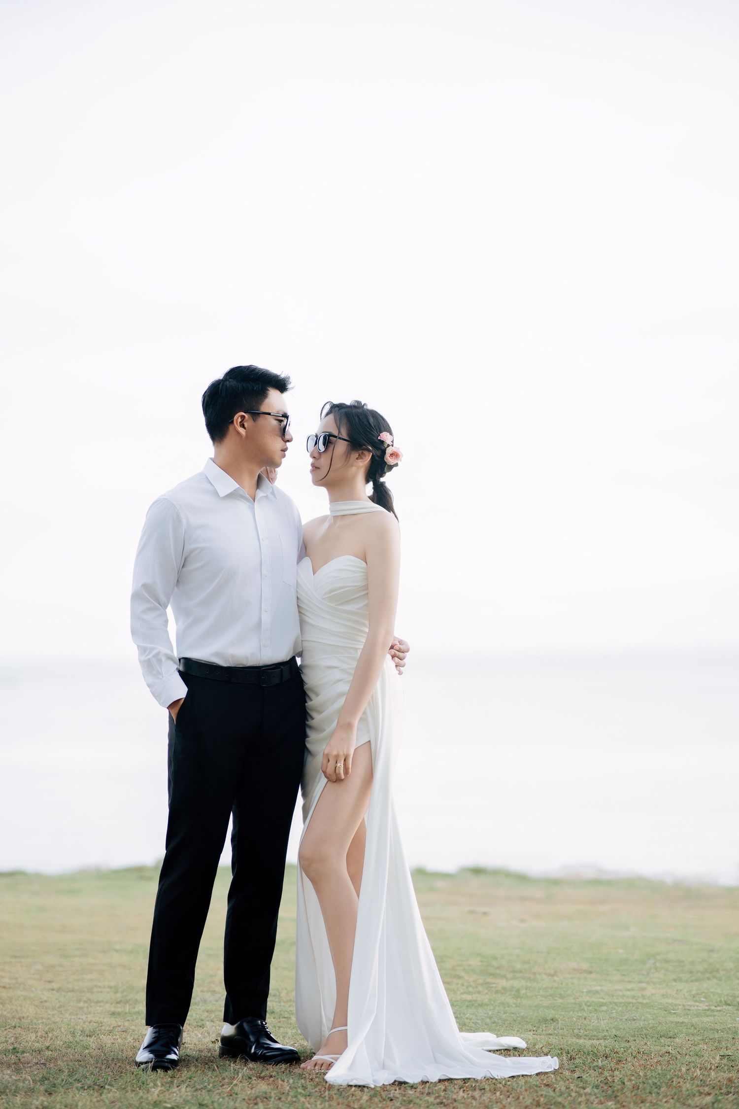 A couple shares intimate moments during their wedding photoshoot on a grassy hill.