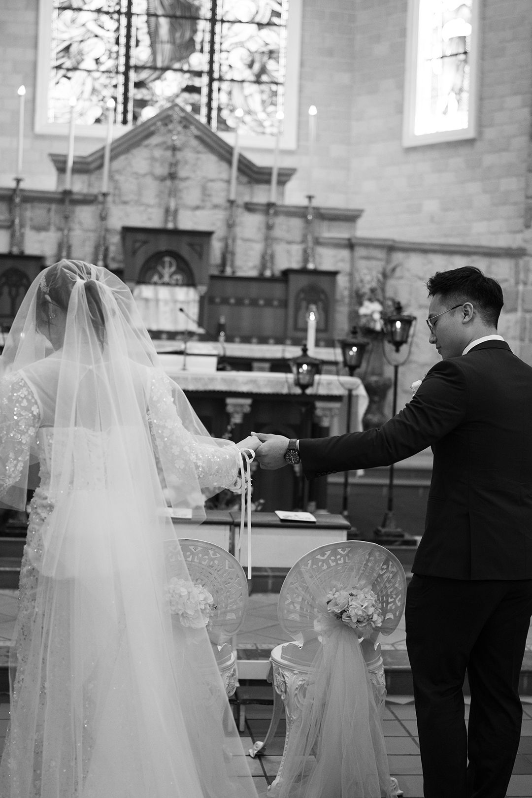 Candid black and white moment of a couple holding hands at the altar in a traditional church wedding ceremony