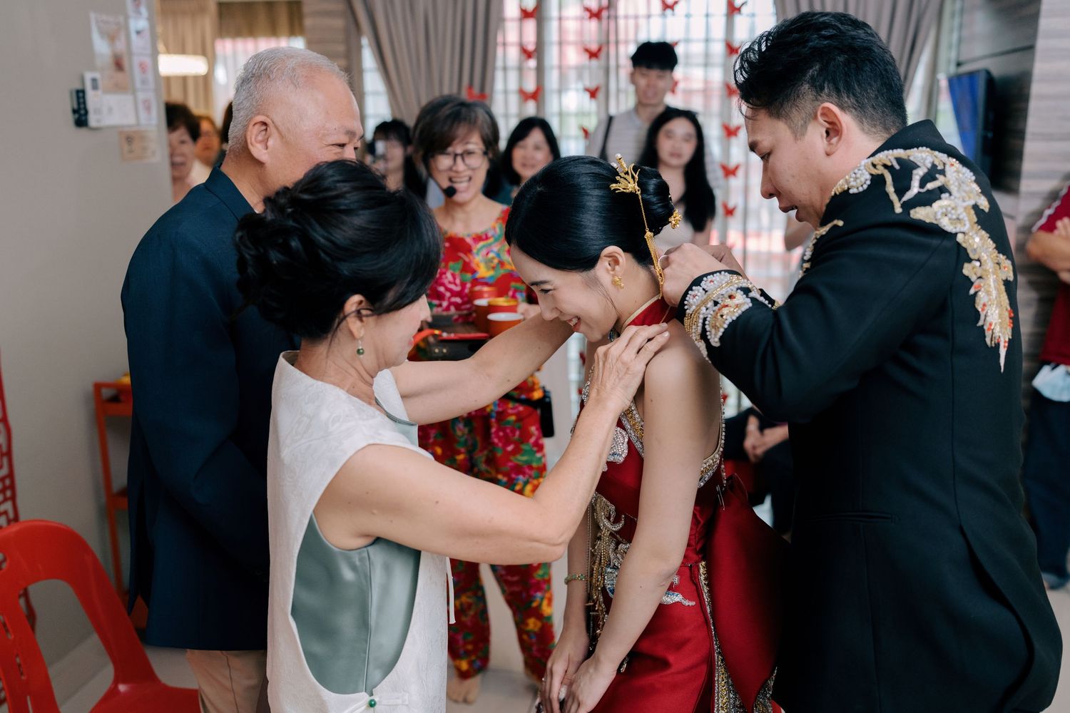 The bride smiles as her family adorns her with traditional gold jewelry during her wedding day