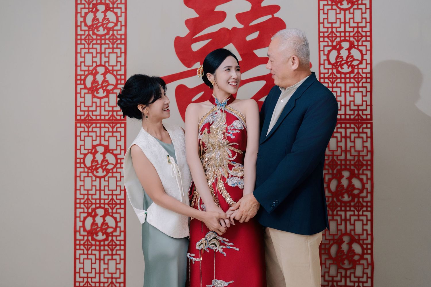 Bride in traditional Chinese wedding attire shares a joyful moment with her parents during the tea ceremony