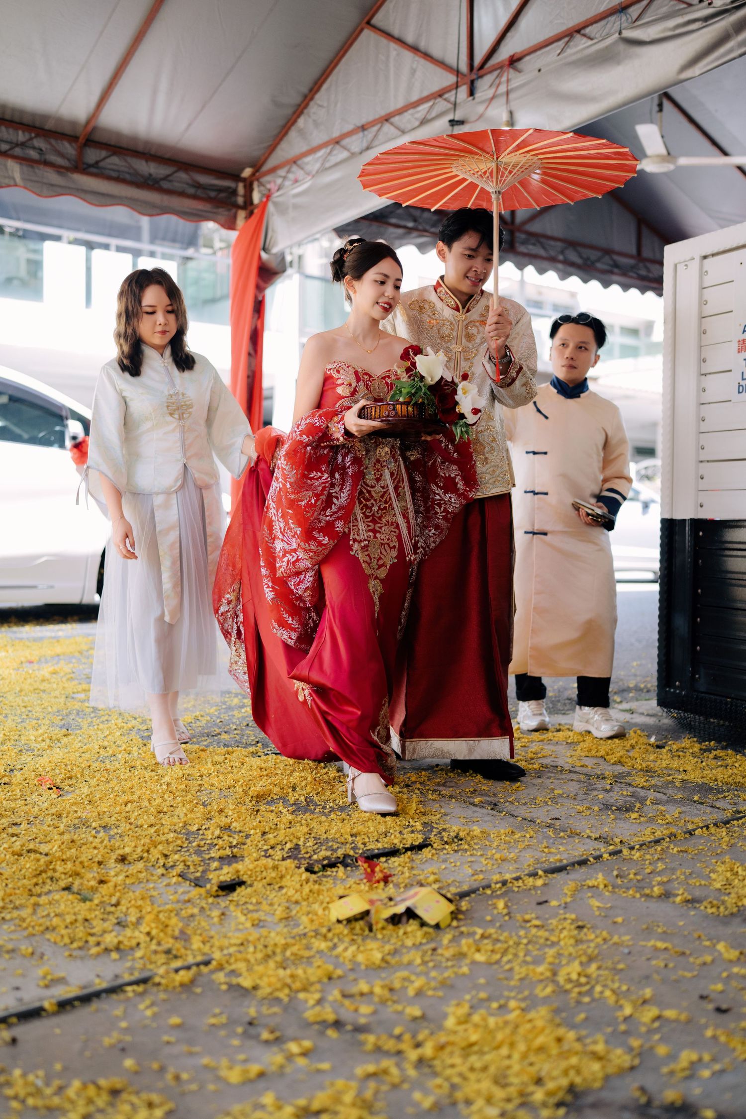 Traditional Asian wedding ceremony with red parasol and yellow flower petals scattered on the ground.