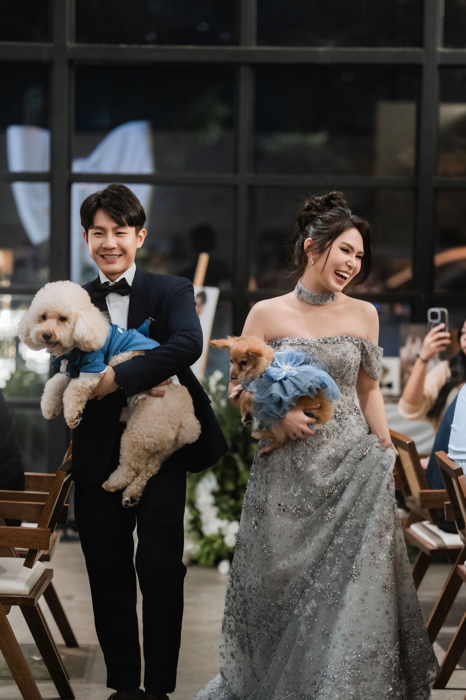 A couple holds their small white dog during their wedding celebration in formal attire.