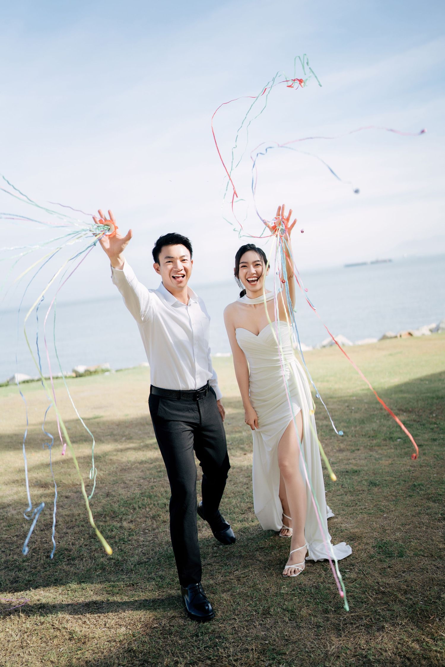 A couple celebrates with streamers on a hilltop in elegant white and black formal attire.