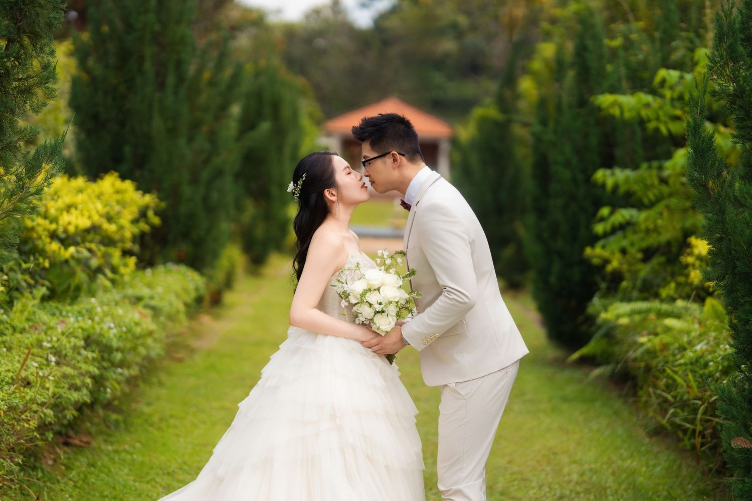 Wedding couple shares romantic moments along a garden path surrounded by greenery.