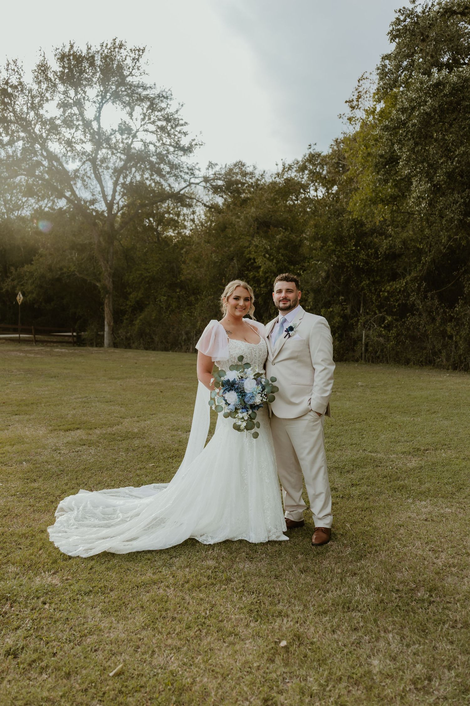 Wedding couple posing in a grassy field with natural landscape backdrop.