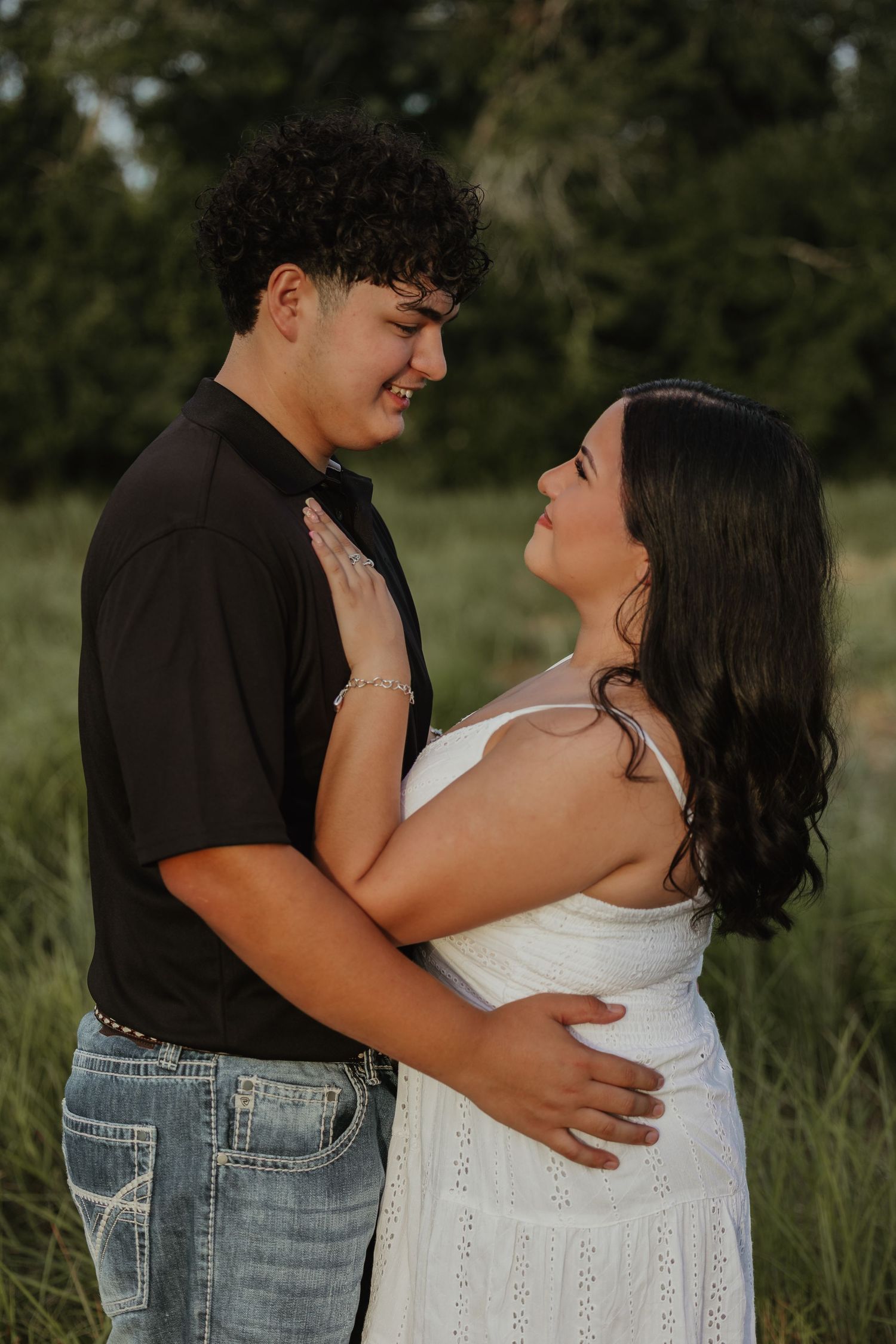 Tender embrace between couple in casual outfits against natural outdoor backdrop.