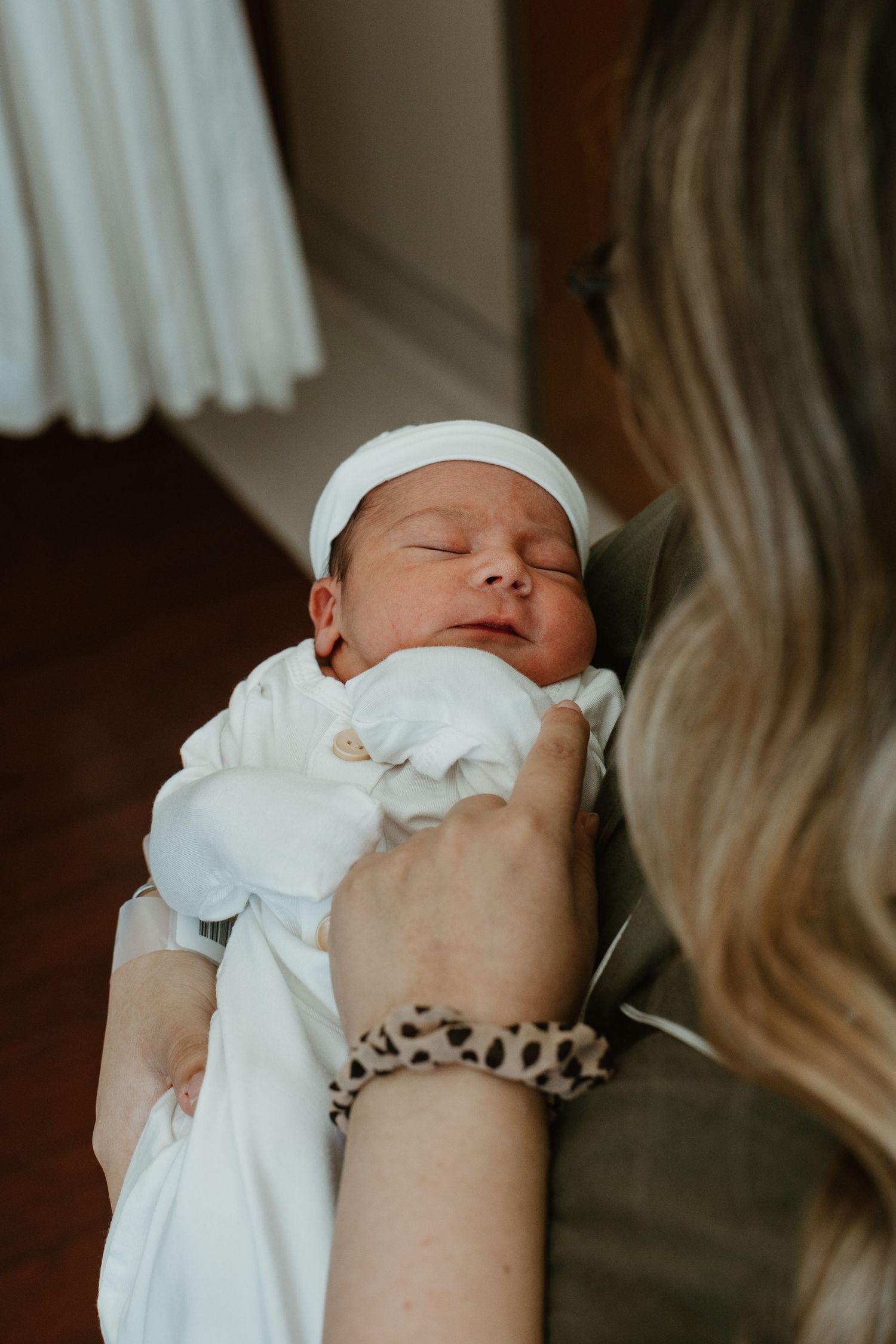 Sleeping newborn wrapped in white swaddle being held against first time mom's chest.