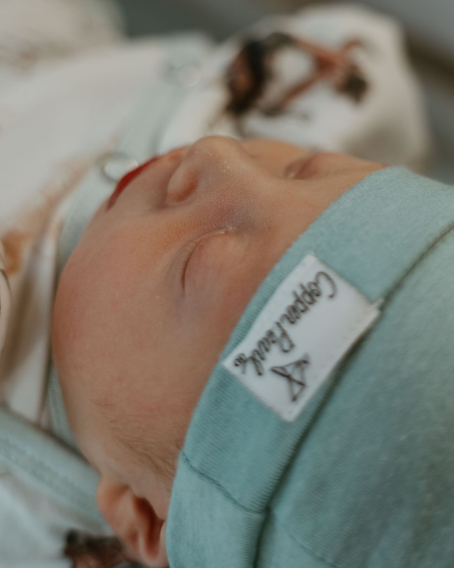 Close-up of a newborn baby wearing a hospital identification bracelet and mint green swaddle.