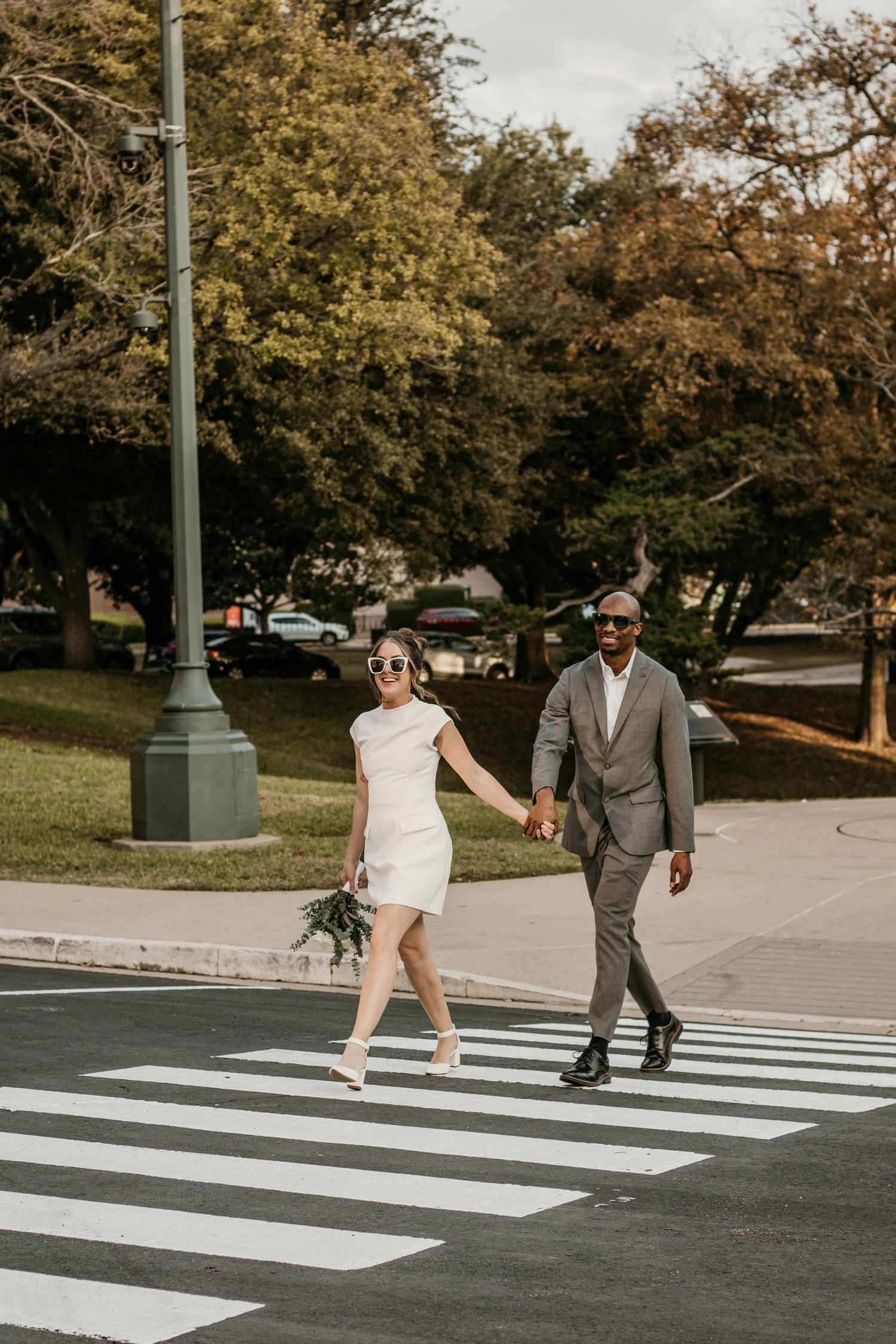 A couple in formal attire walks across a crosswalk during a photo session.