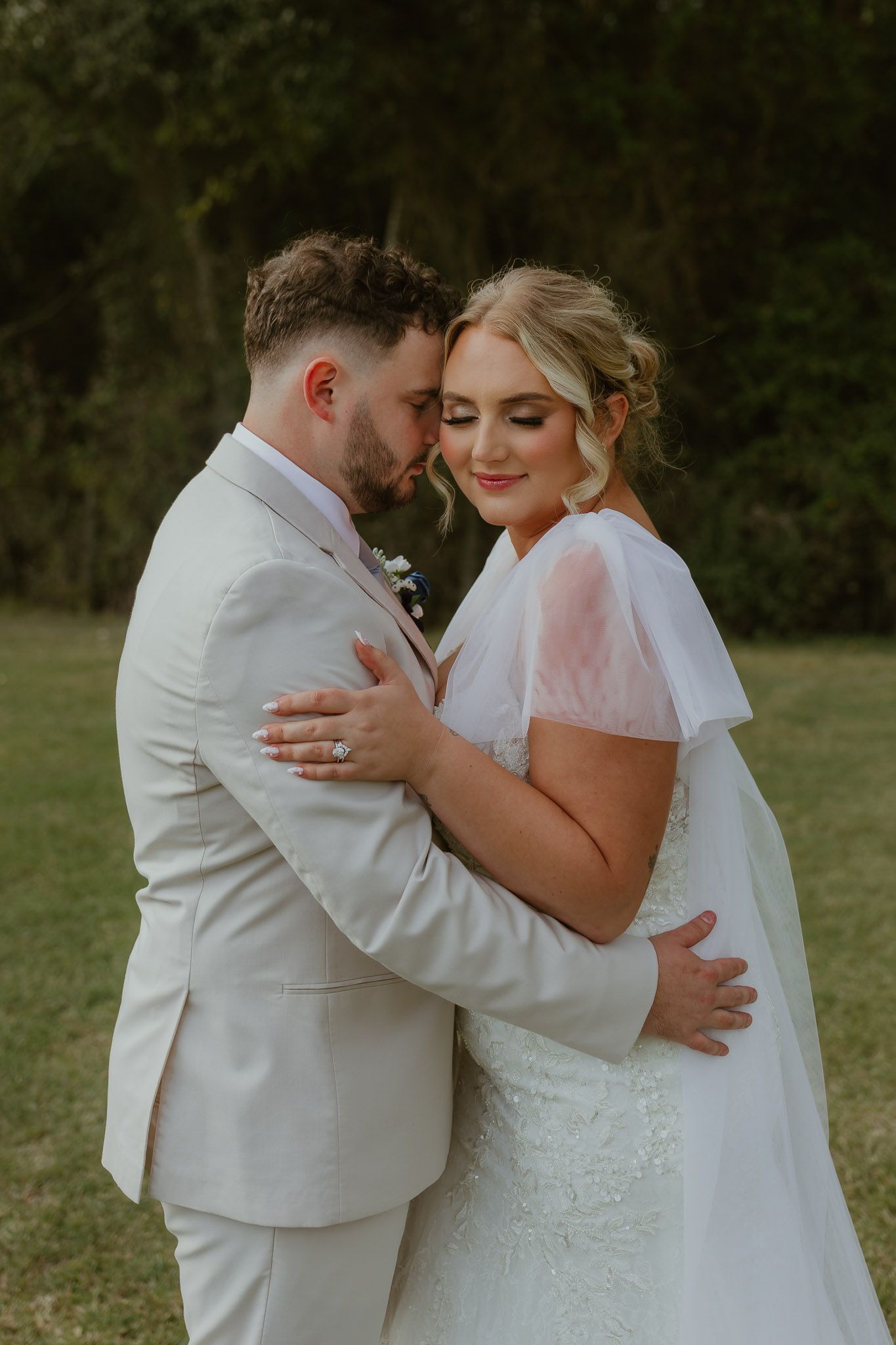 A romantic moment between newlyweds in white attire embracing outdoors during their wedding photoshoot.