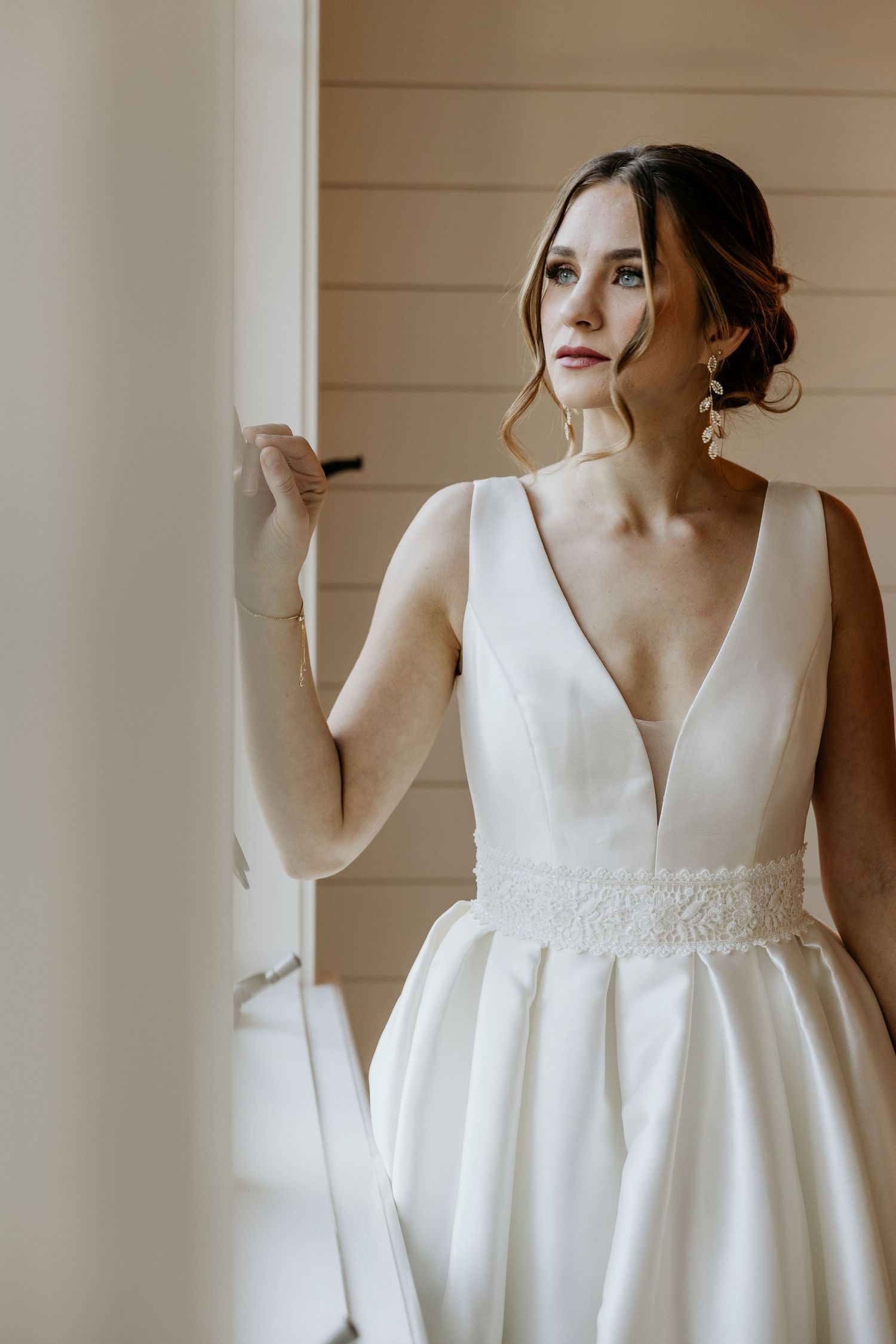 A wedding dress with a plunging v-neckline and beaded waistline detail is showcased against a neutral background.