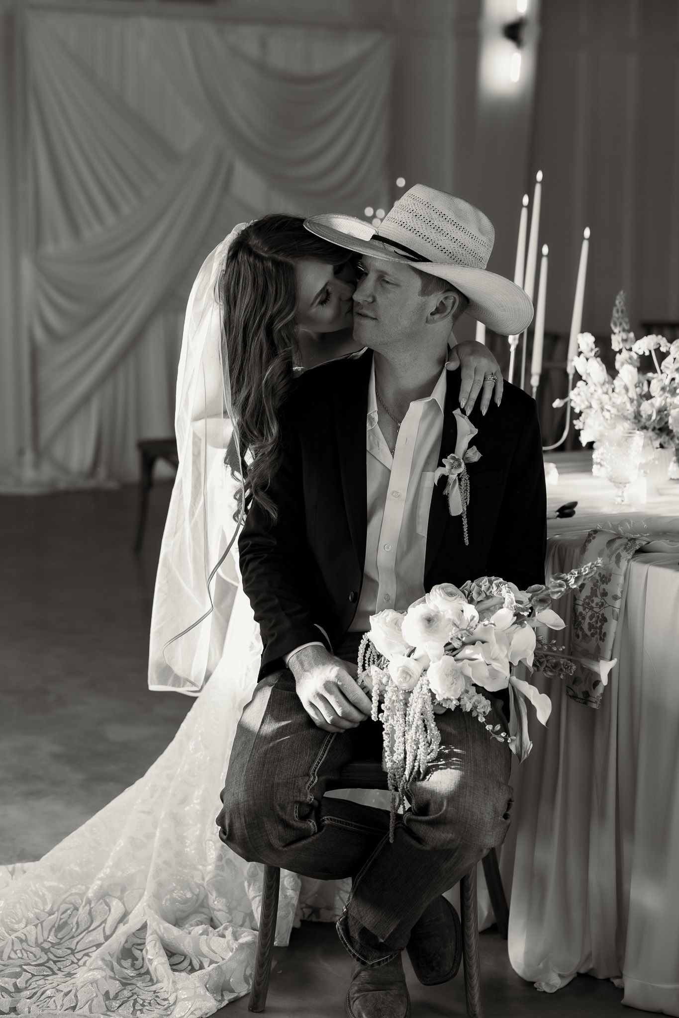 Black and white photo of a bride and groom sharing a romantic moment, groom wearing a cowboy hat at their wedding reception.