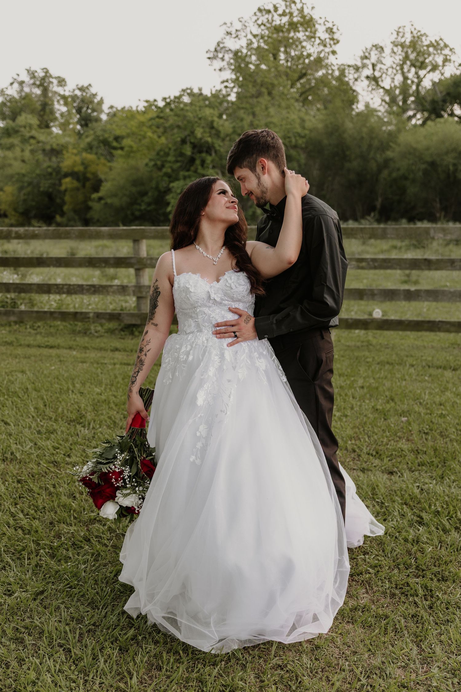 Newlyweds sharing intimate moment in grassy field with white wedding dress.