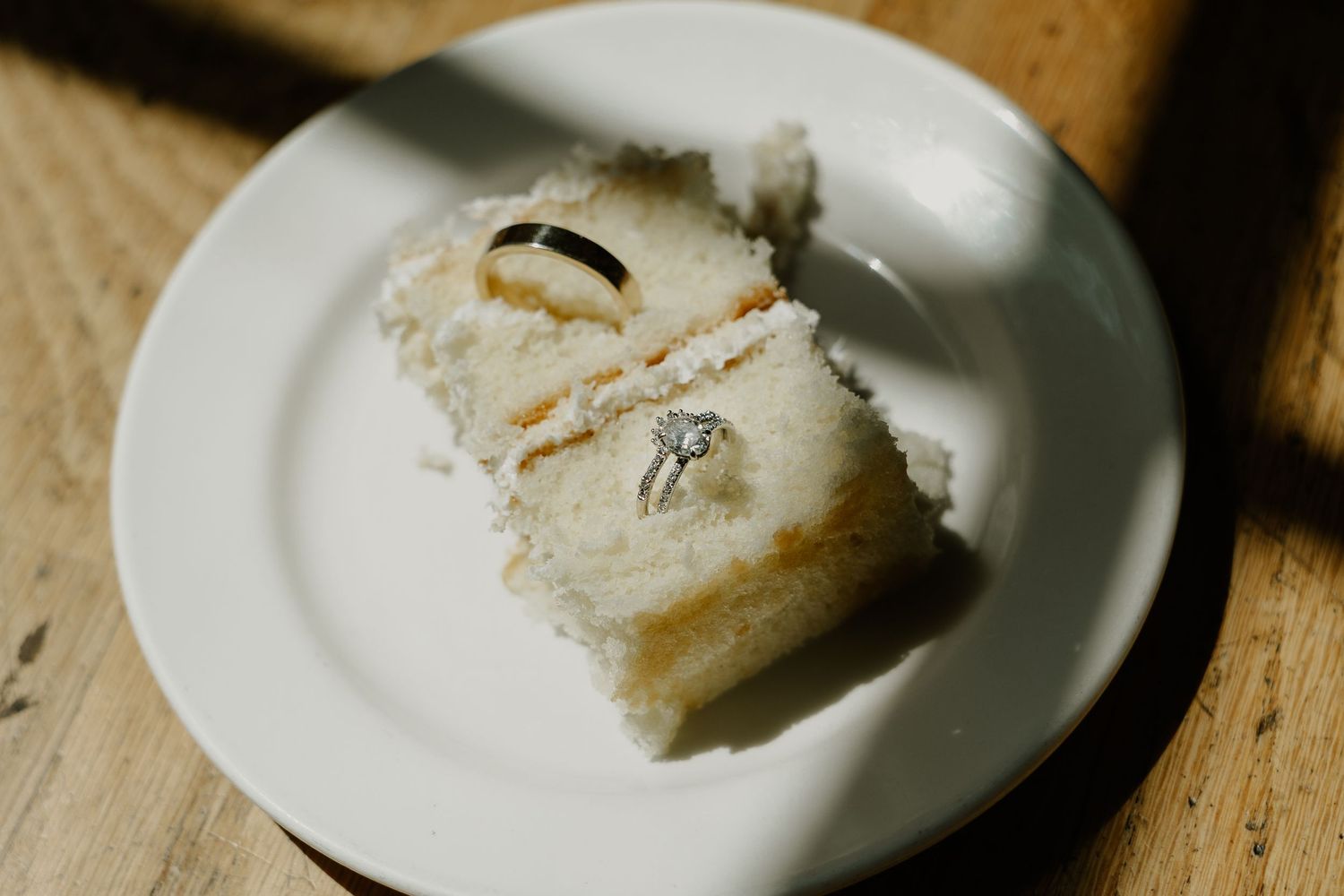 A slice of white wedding cake with filling on a simple white plate.