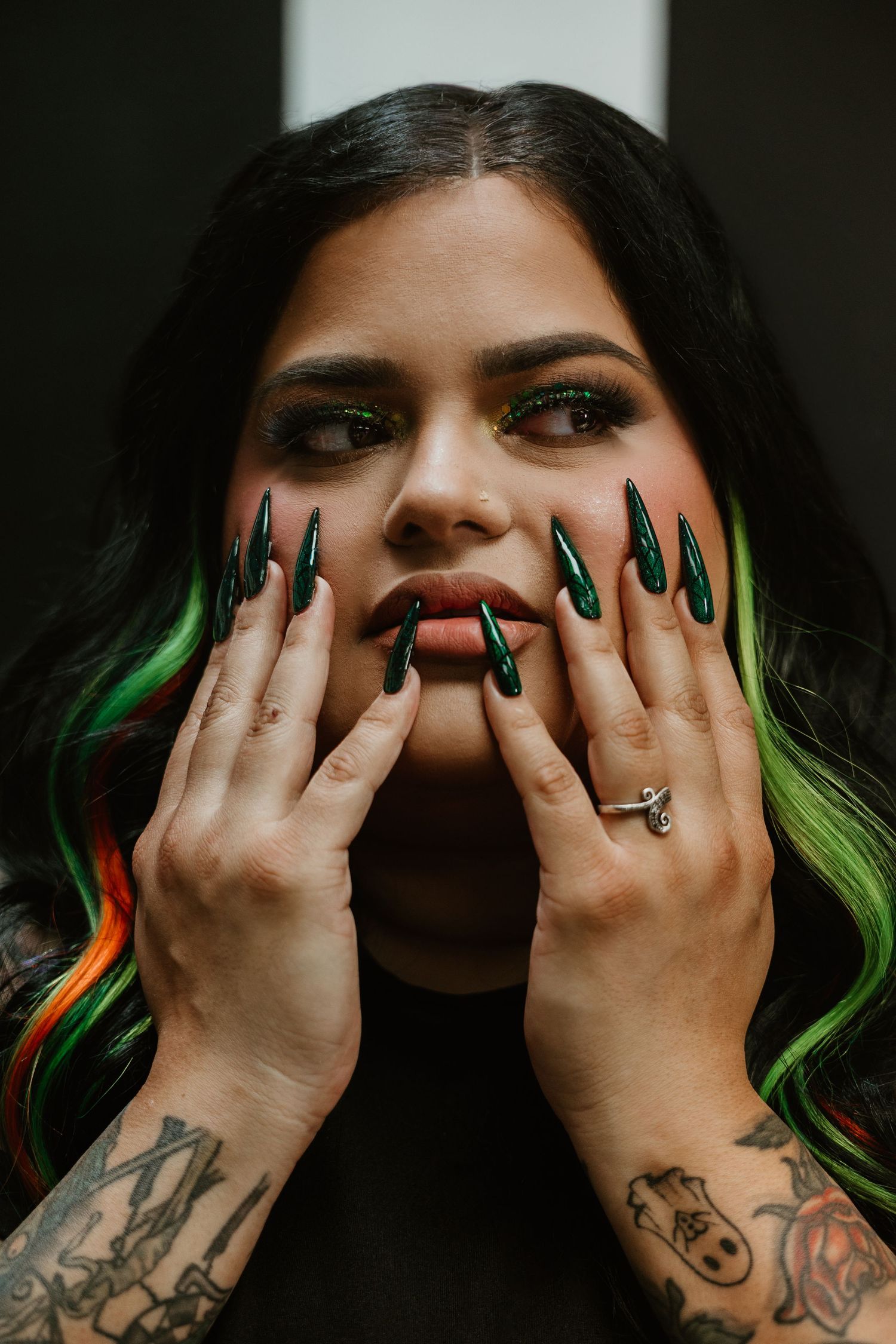 Artistic nail photography featuring green chrome nails and tattoos against dark background.