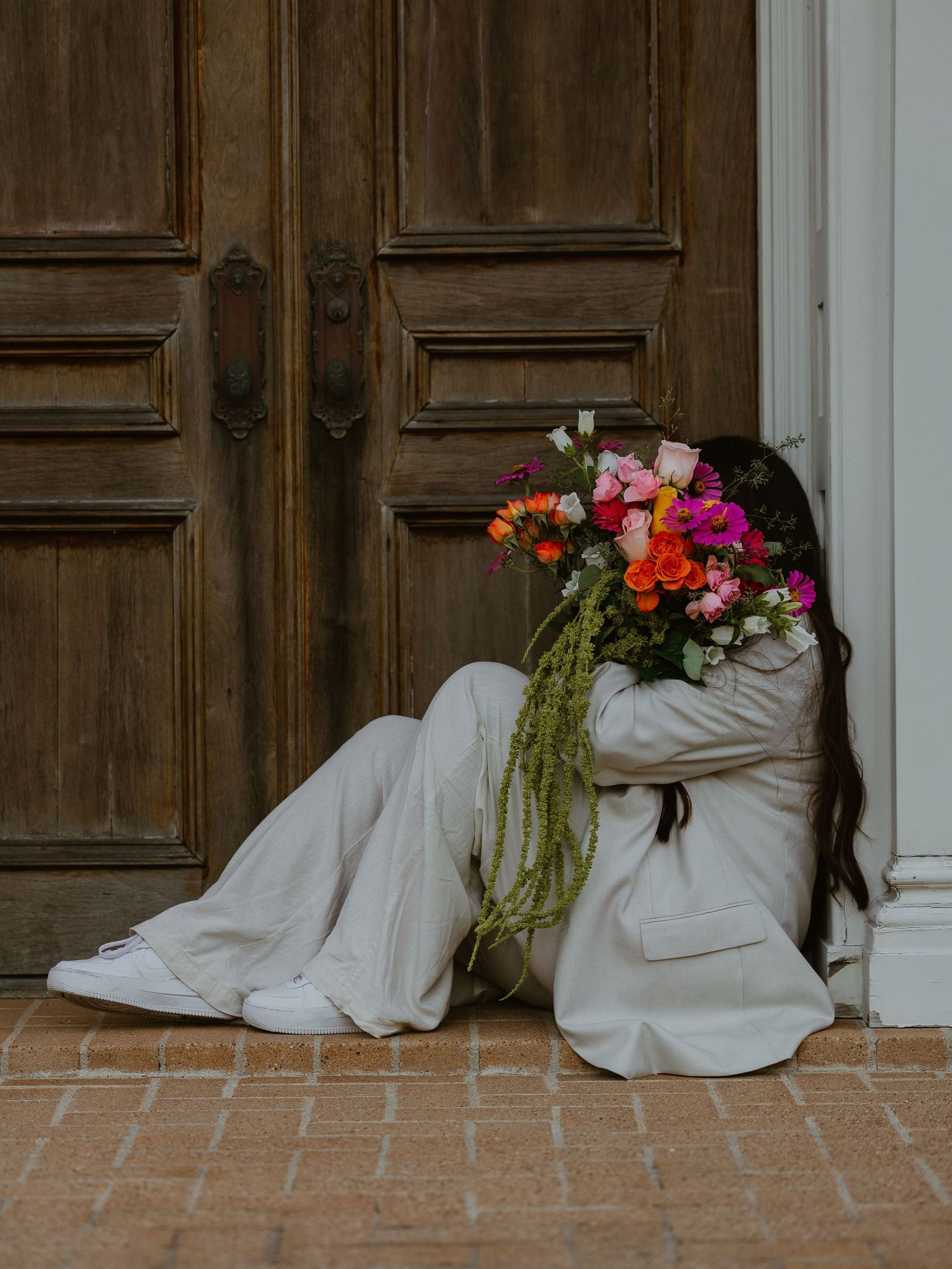 Low angle shots showing white suit and floral bouquet against wooden door backdrop.