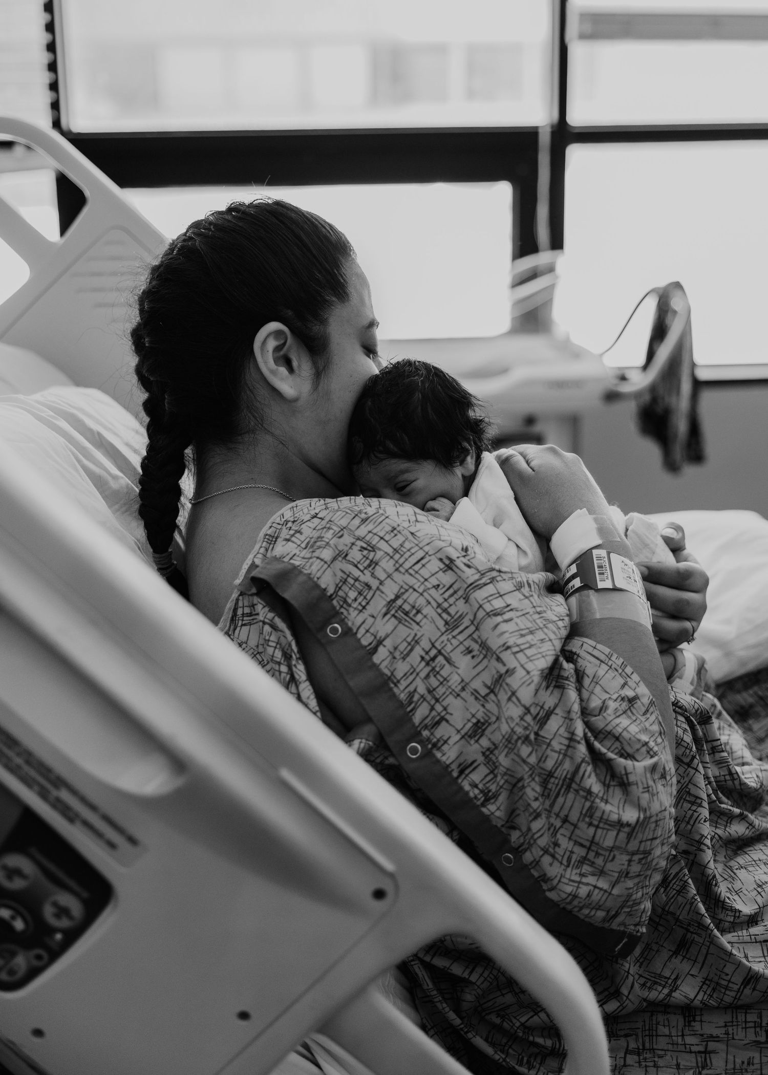 Black and white photo of a new mother in a hospital gown cradling her newborn baby while sitting in a hospital bed.