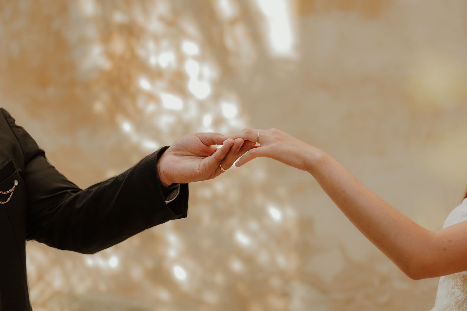 A couple holds hands during a romantic outdoor photoshoot with soft sunlit bokeh in the background.