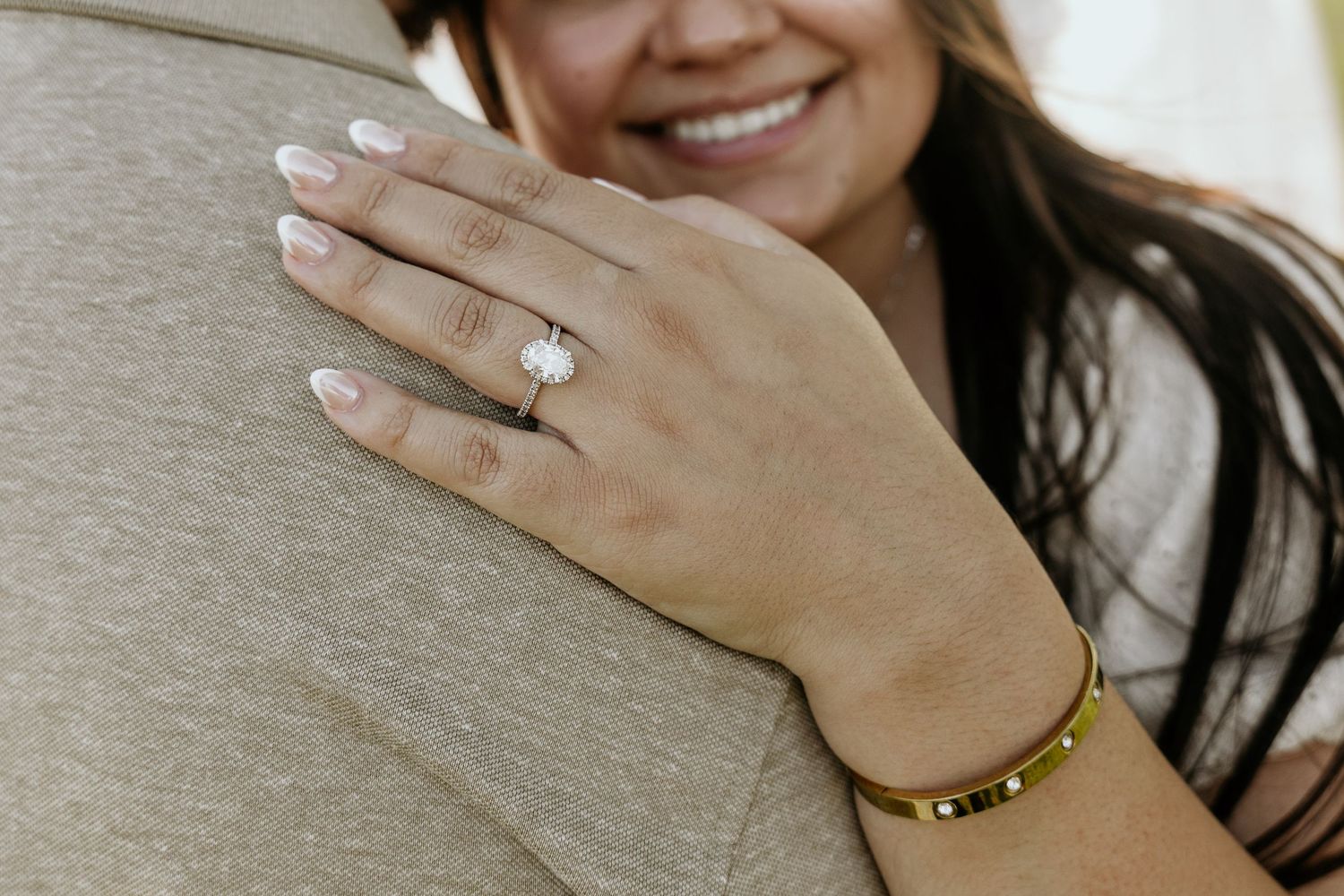 Close-up shot showing hands with engagement rings against a neutral background.