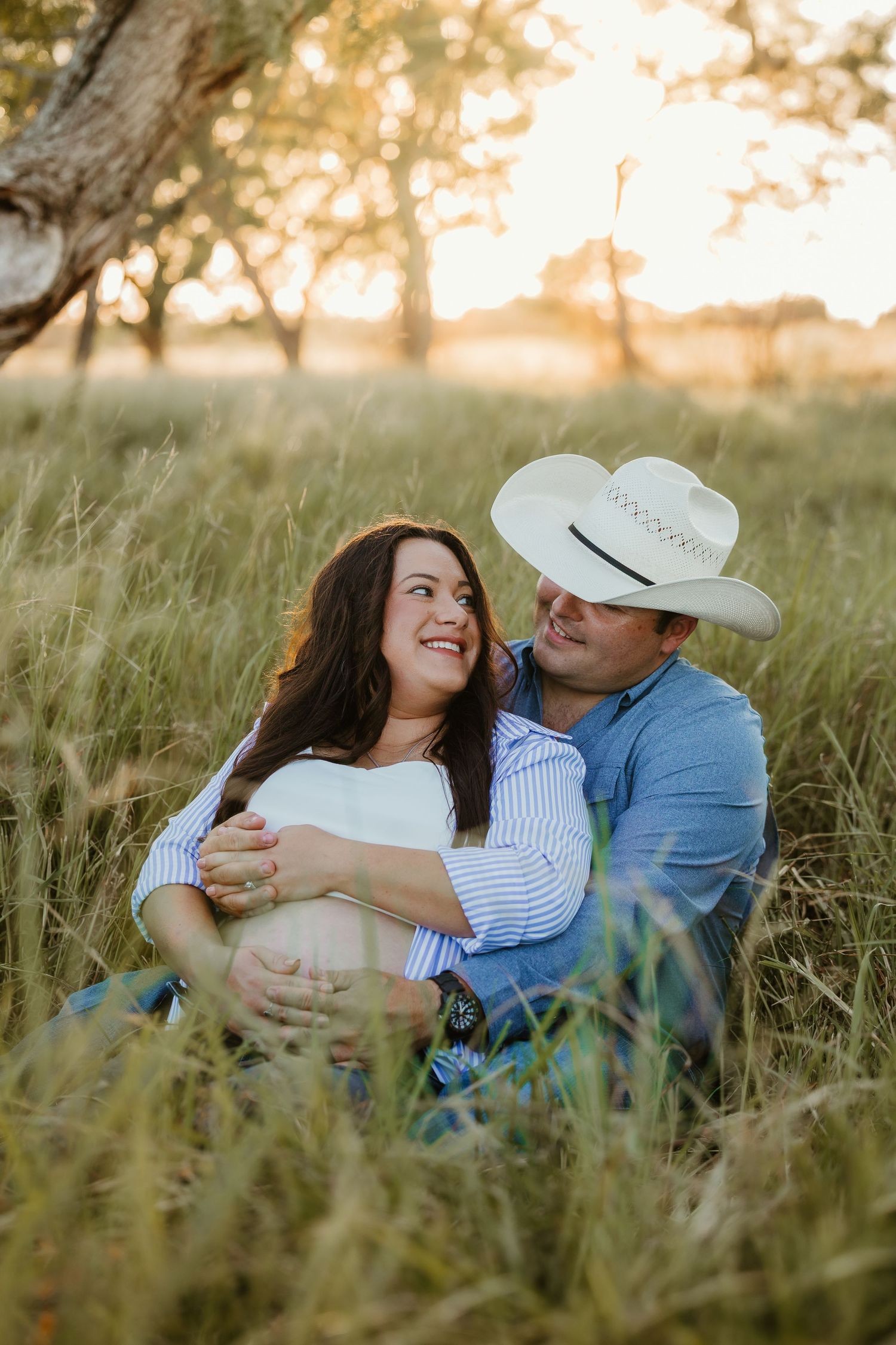 A couple shares a romantic moment lying in tall grass during golden hour sunset.