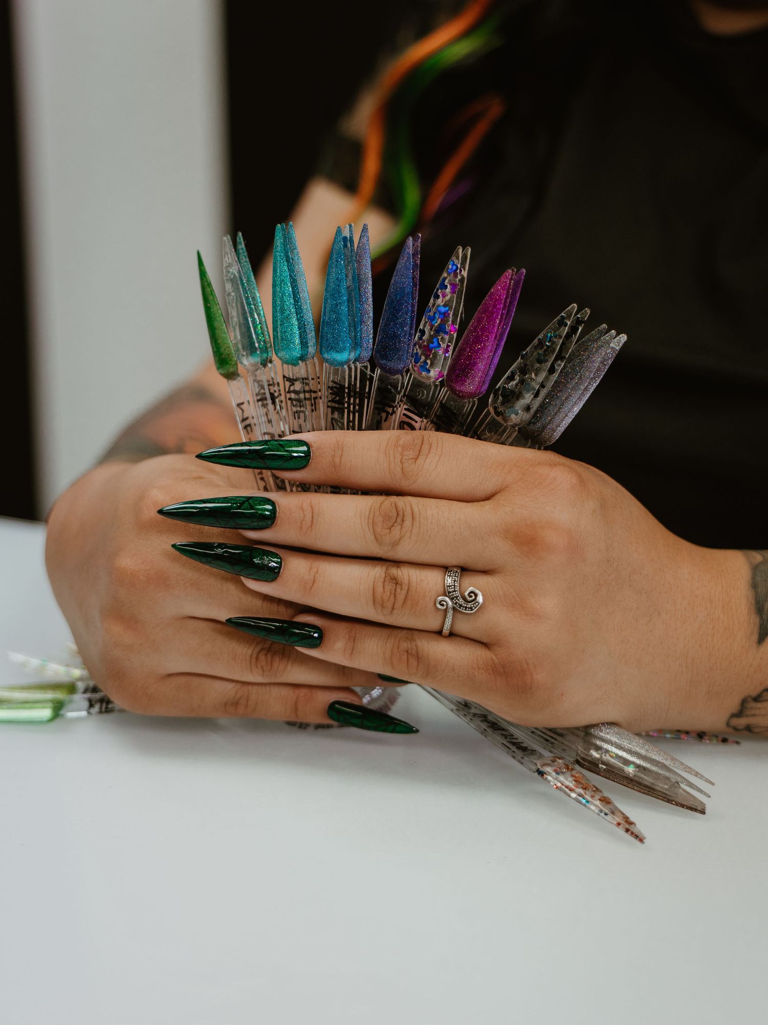 Close-up of hands with long green metallic nails and colorful nails arranged artistically.