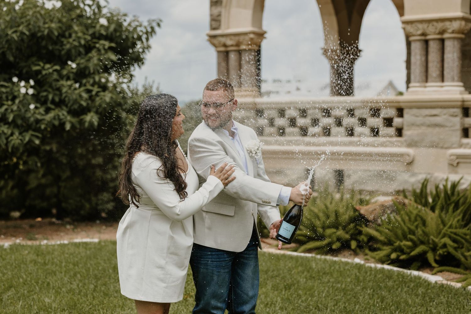 A couple poses for wedding photos in front of a grand architectural backdrop with columns.