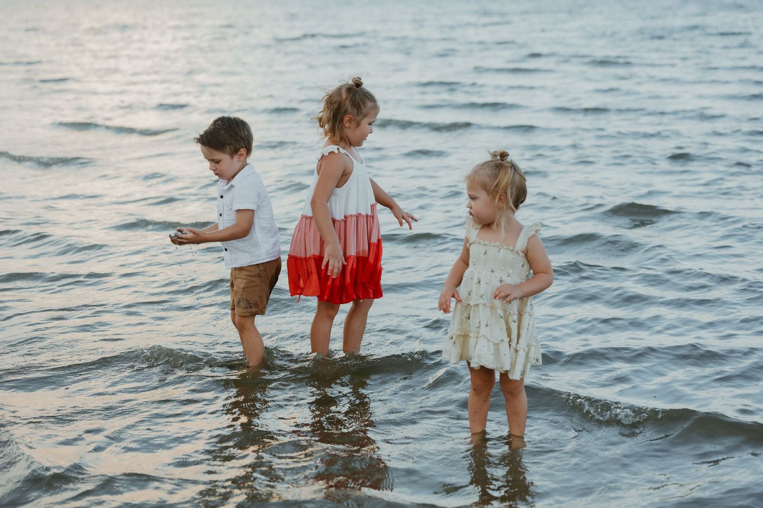 Children play and splash in shallow ocean waters during sunset.