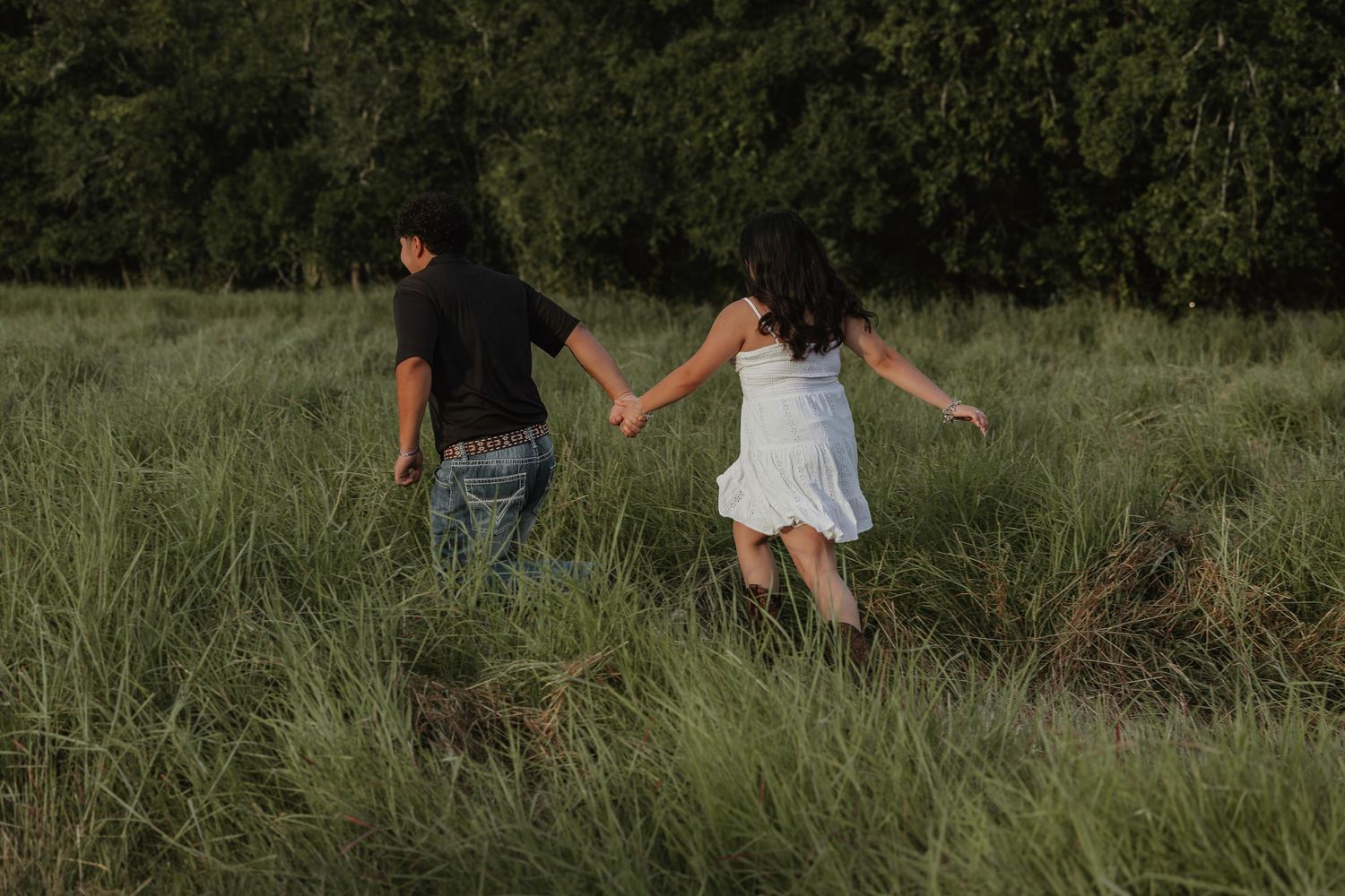 Romantic couple walks hand in hand through tall grass at golden hour.
