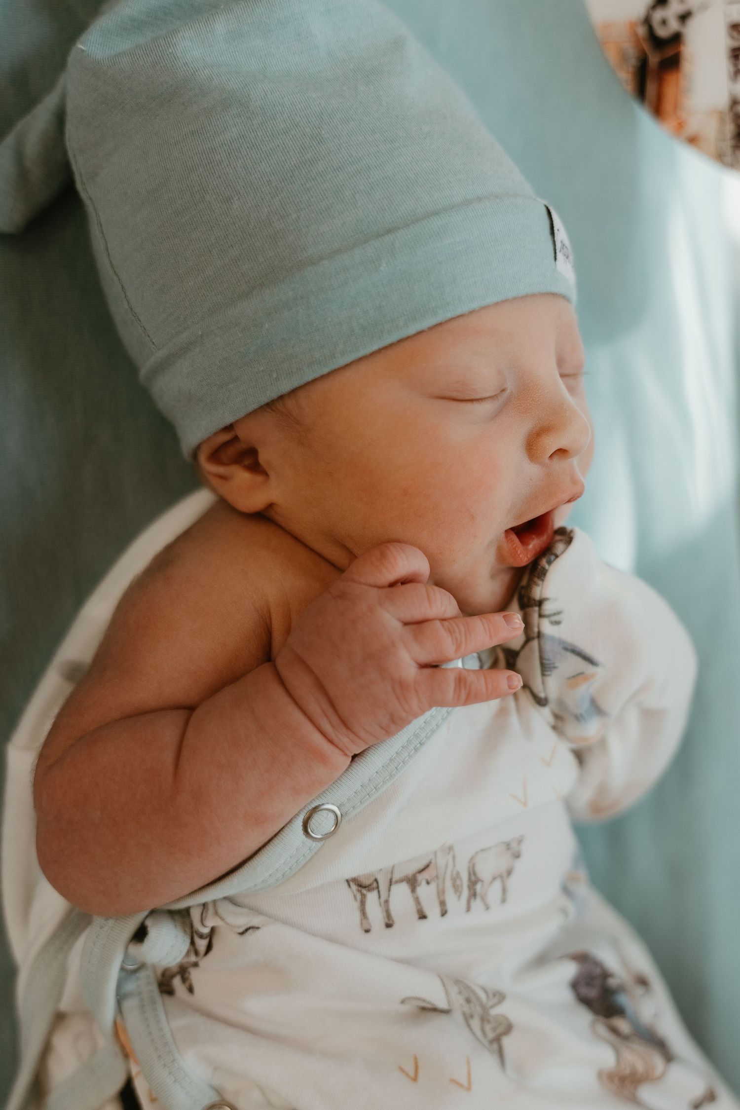 Close-up of peaceful newborn baby wearing mint green cap.