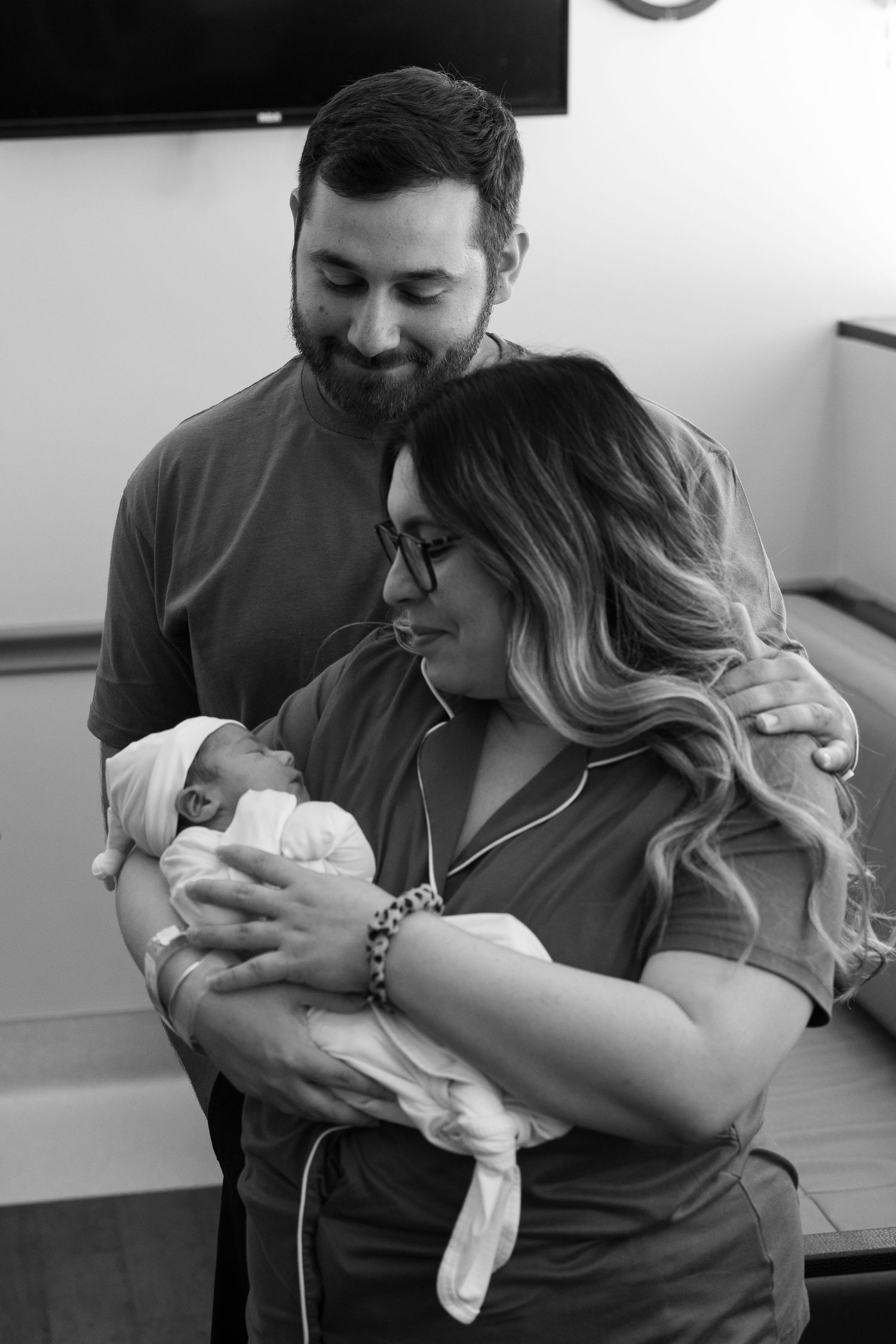 Black and white photo of parents cradling their newborn baby in hospital room.
