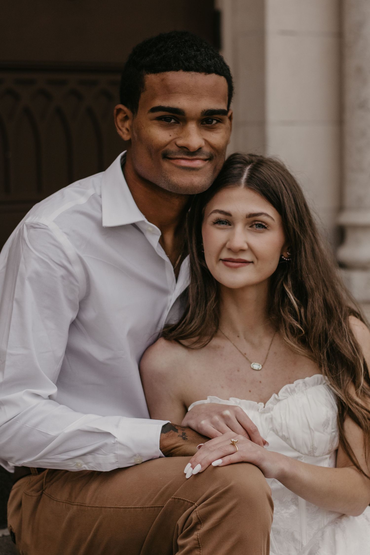 Romantic couple in white and brown clothing embracing during engagement photo shoot.