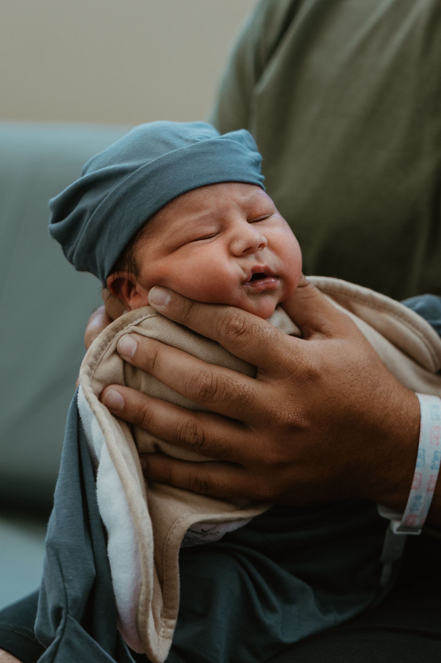 Gentle hands cradling a sleeping newborn in blue hat.