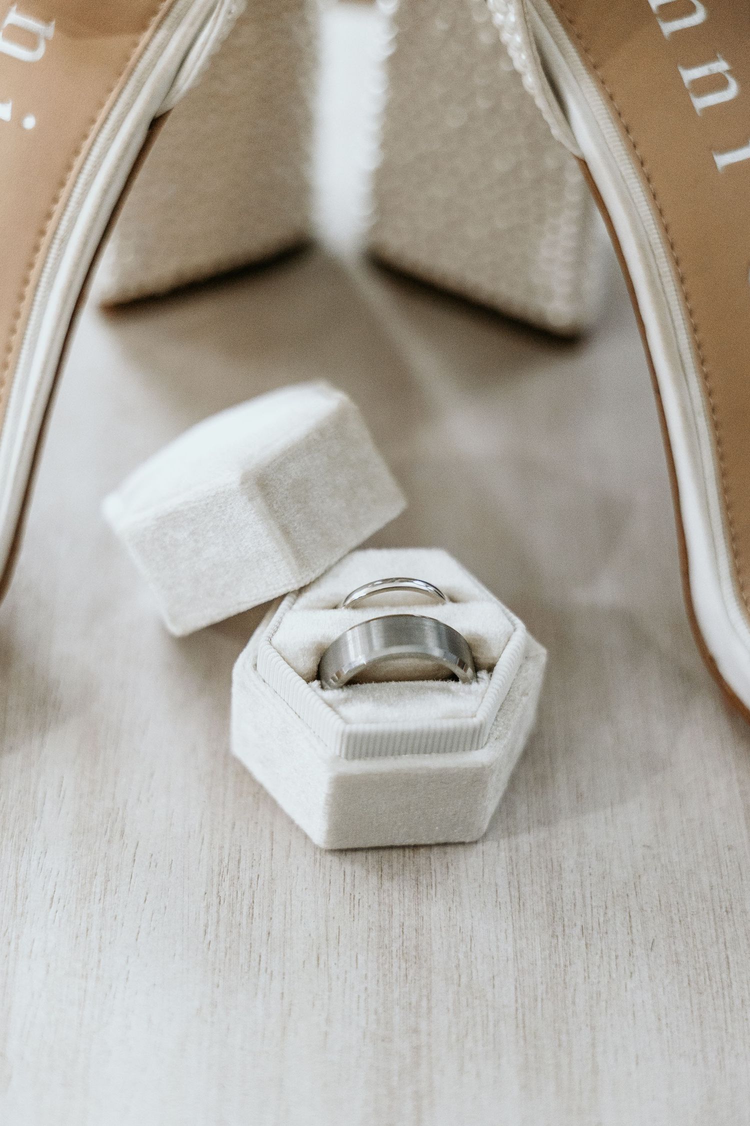 Wedding ring in a white hexagonal velvet ring box next to a wedding shoe.