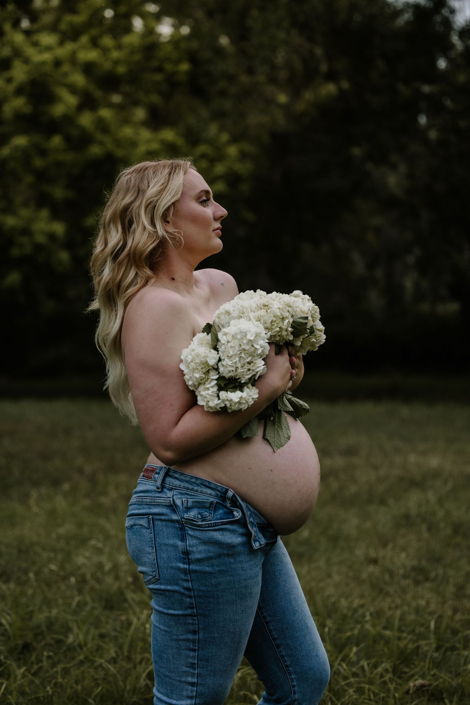 A maternity photo featuring white hydrangea flowers outdoors with greenery.