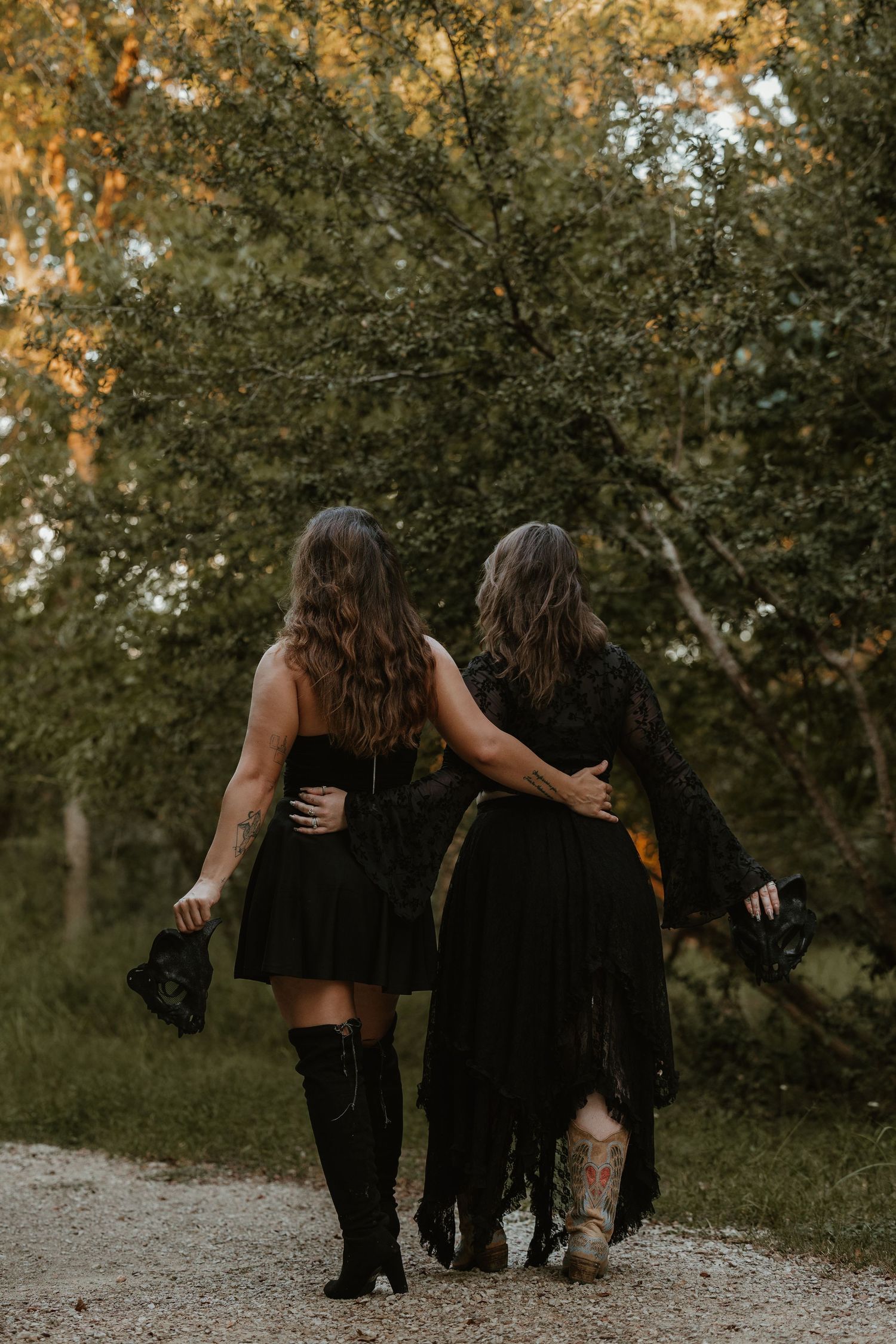 Friends in black dresses walk together on forest path during golden hour.