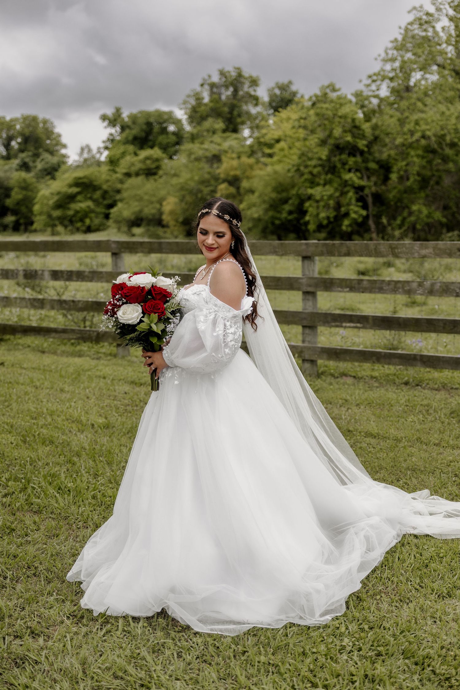 Bride in white dress twirling outdoors with flowing veil and red bouquet.