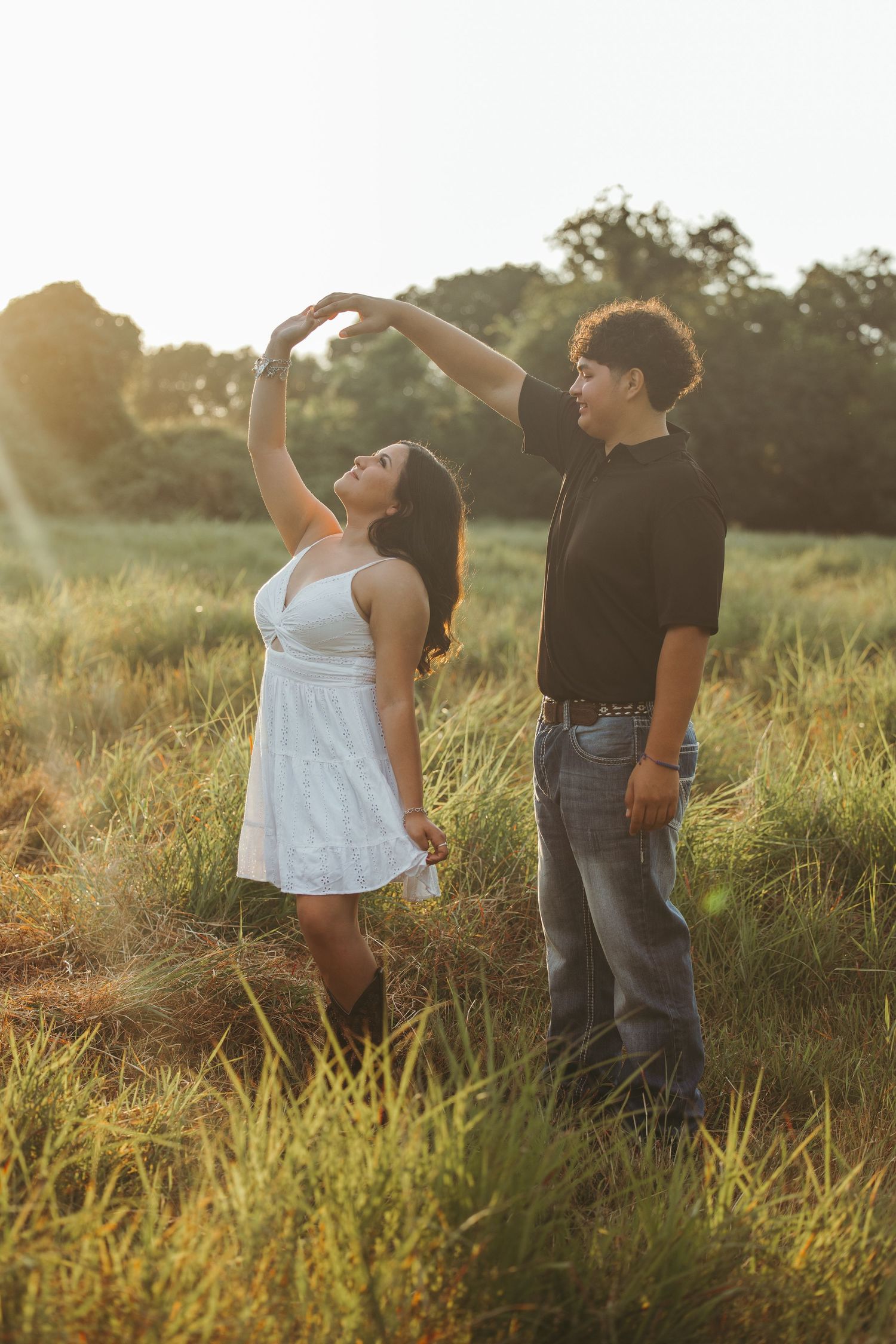 Joyful couple poses expressively in sunlit meadow during photo session.