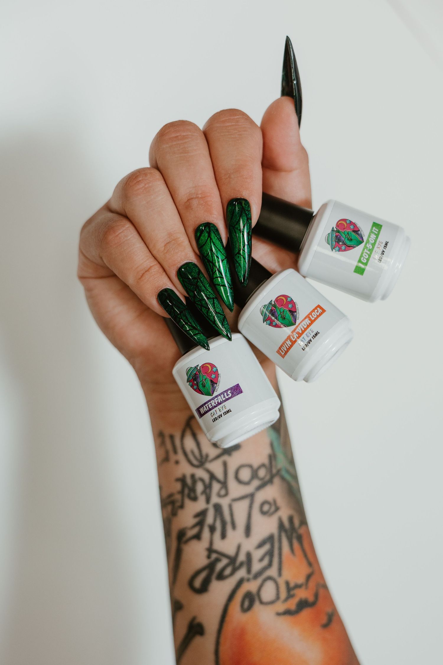 Nail artist hand holding nail polish bottles displaying green spiderweb chrome manicure.