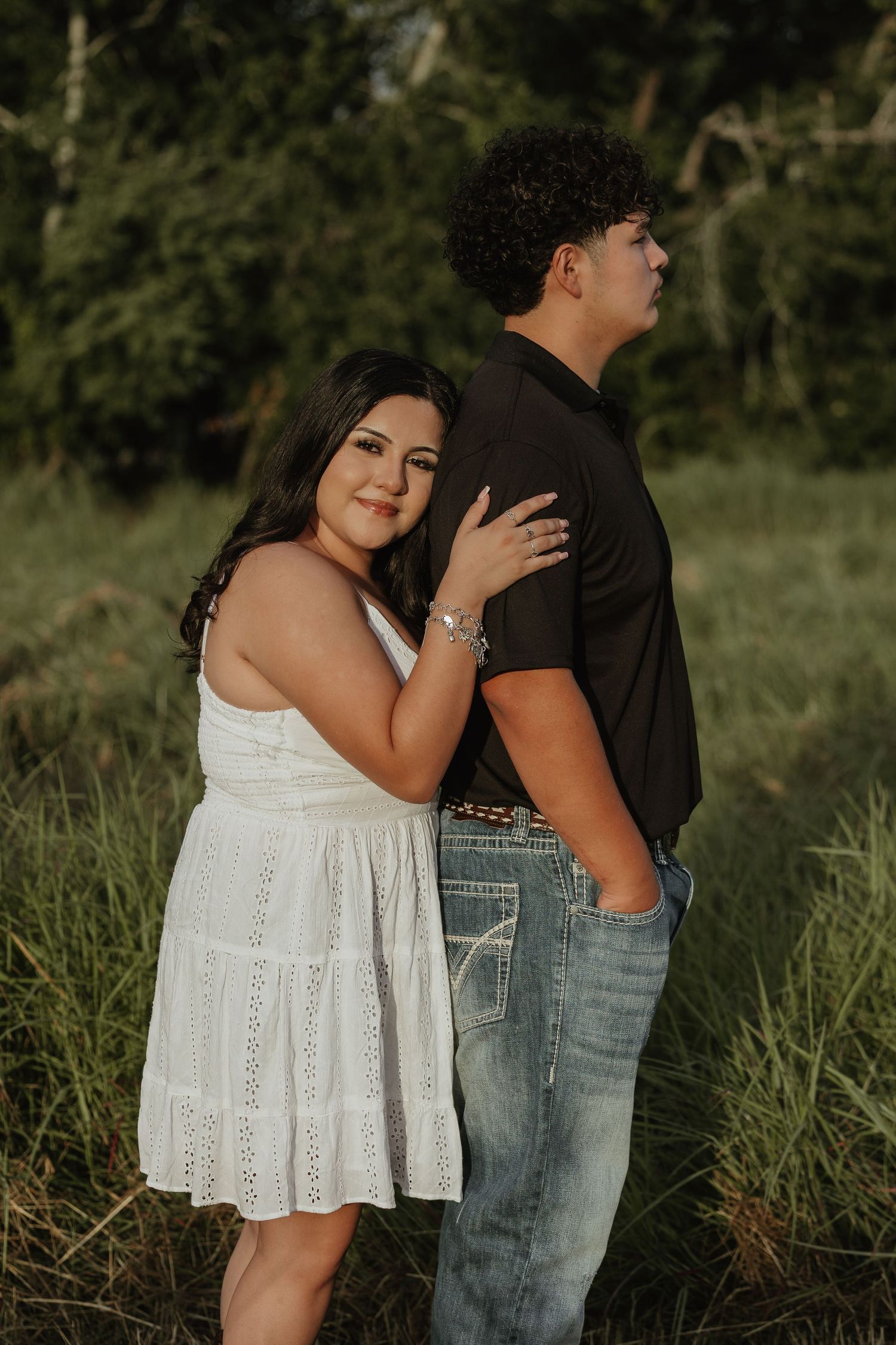 Couple poses intimately in a grassy field during sunset photoshoot wearing white dress and black shirt.