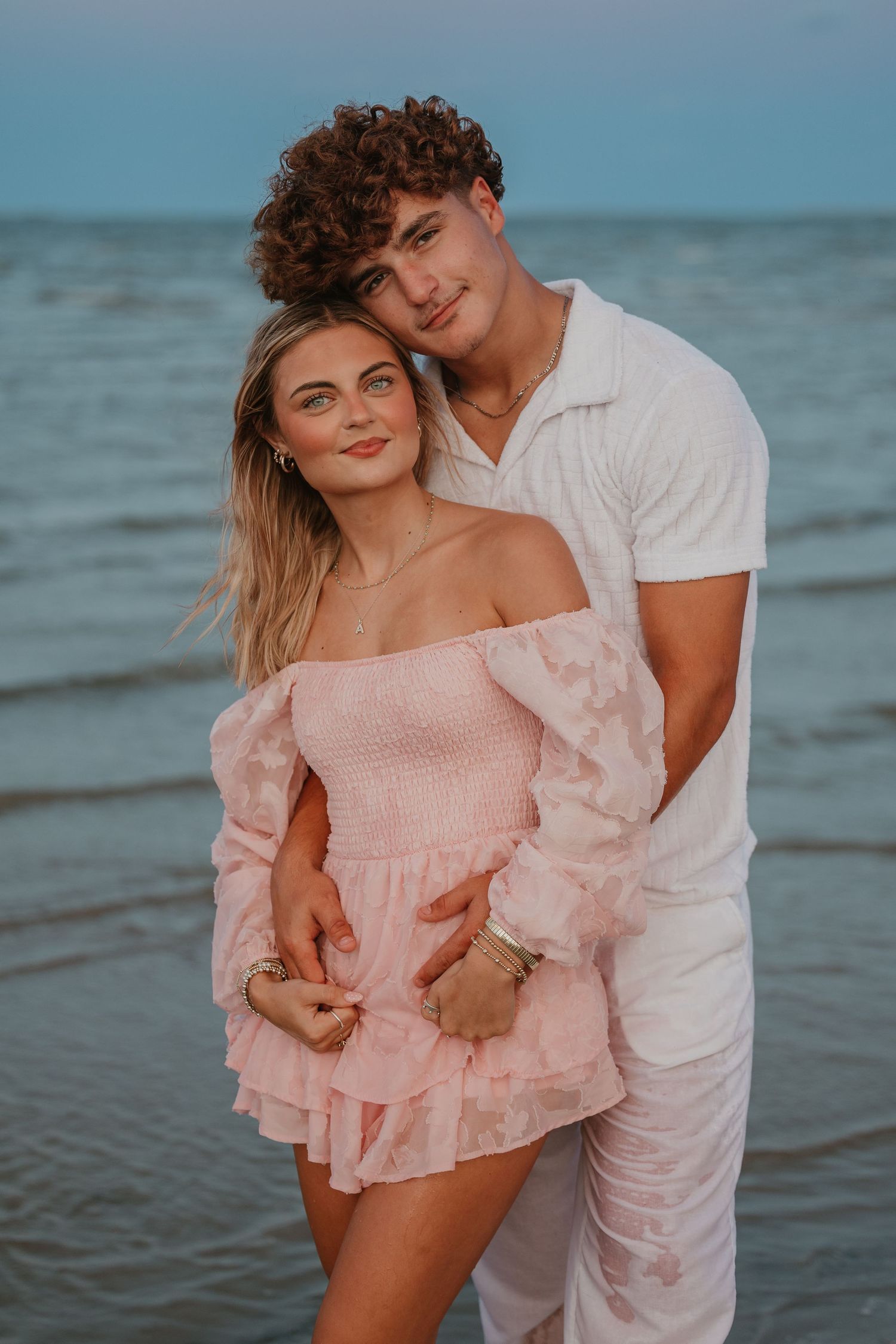 An intimate beach portrait of a couple in coordinated pink and white outfits.