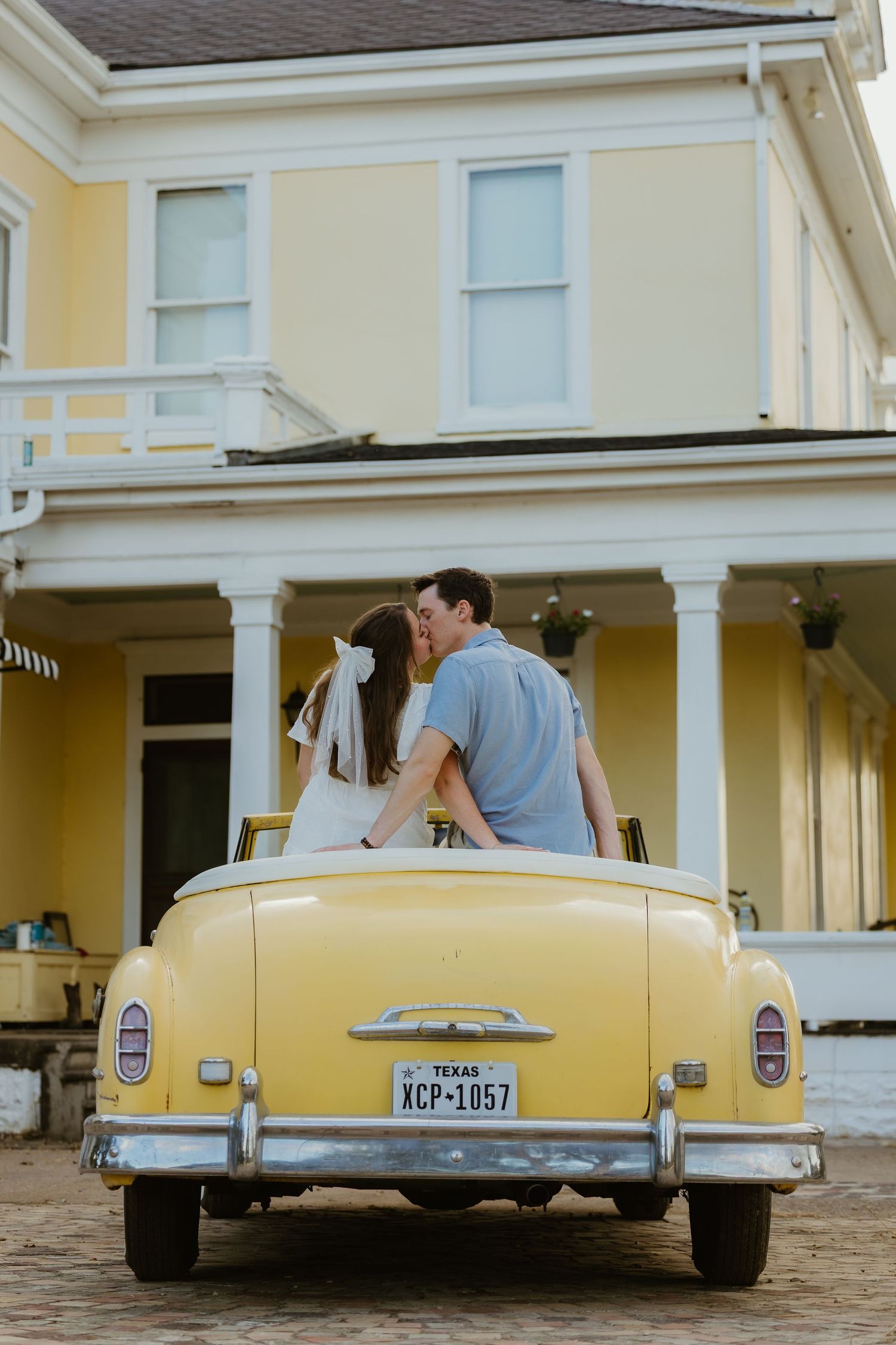 A couple shares an intimate moment while sitting on a yellow vintage car.