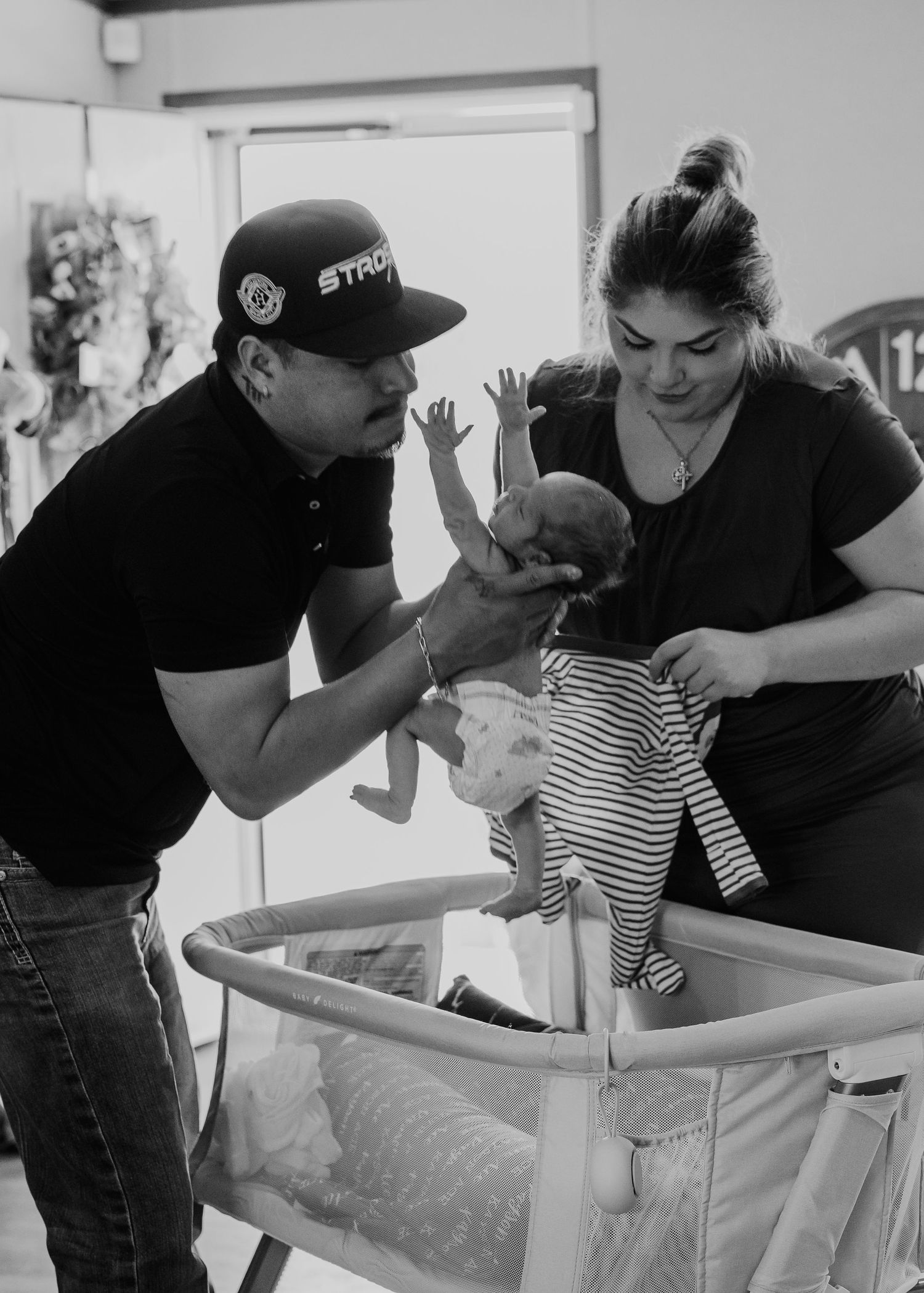 Black and white photo of two parents lovingly holding their newborn baby over a white crib.