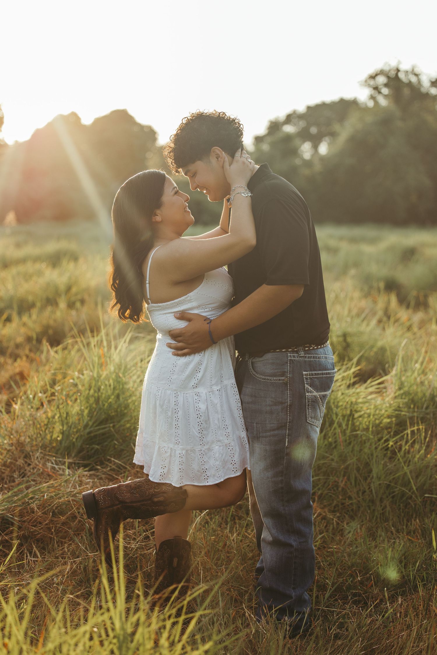 Couple shares playful moments in sunlit field wearing white dress and jeans.