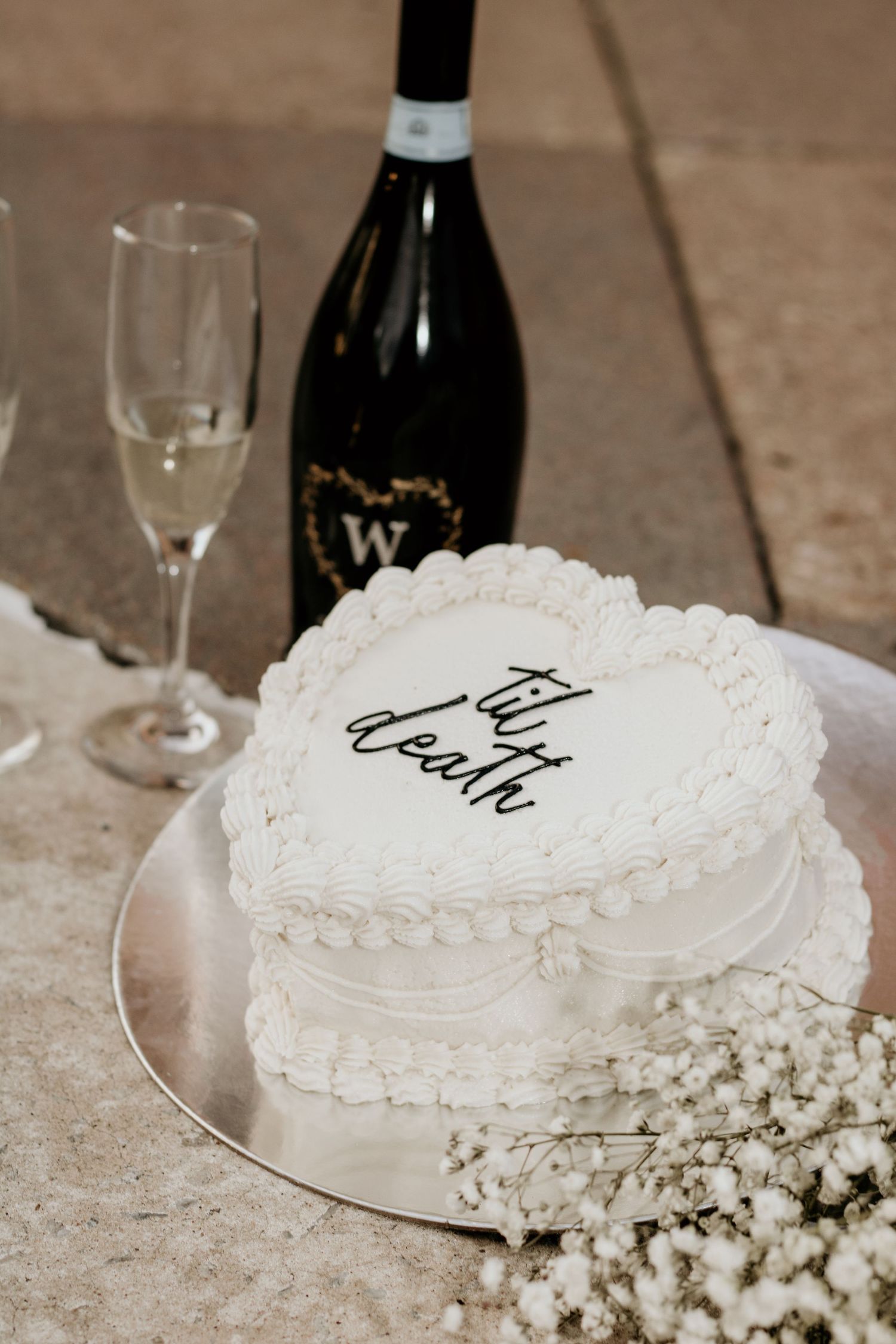 A heart-shaped white wedding cake with delicate frosting details and baby's breath flowers.